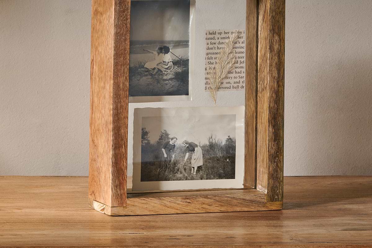 The Indu Standing Mango Wood Frame - Natural by nkuku, crafted from rustic-finished mango wood, displays two vintage black-and-white outdoor photos and text. It stands on a wooden surface against a plain, light-colored wall for added charm.