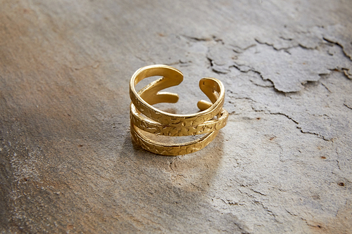 The Katai Ring - Gold by nkuku, featuring a hammered texture and open, layered design, rests on a rugged, stone-like surface.