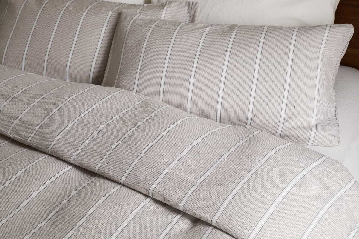 Close-up of a neatly made bed featuring the nkuku Mora Hemp & Cotton Duvet Cover in Stone Grey, paired with two matching pillowcases and crisp white sheets for breathable comfort.