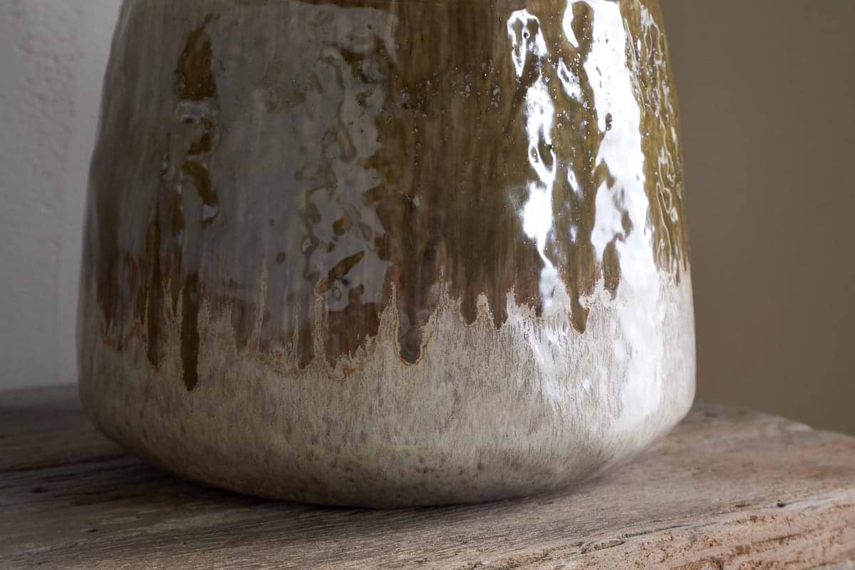 Close-up of the lower portion of the nkuku Melina Reactive Glaze Vase in Olive & Natural, showcasing its glossy finish and textured reflections as it rests on a wooden surface.