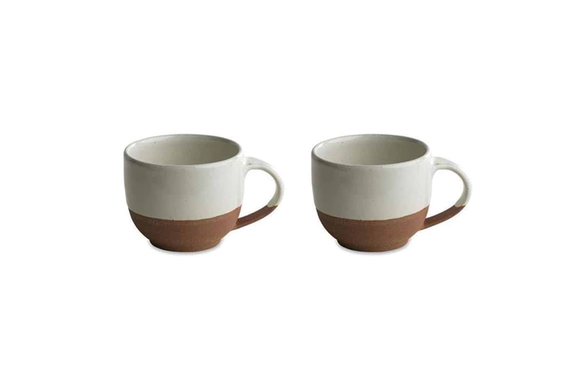 The nkuku Mali White and Terracotta mugs feature a minimalist design with an off-white glazed top and handmade terracotta base, combining rustic charm and modern style. Set of two mugs shown on a white background.