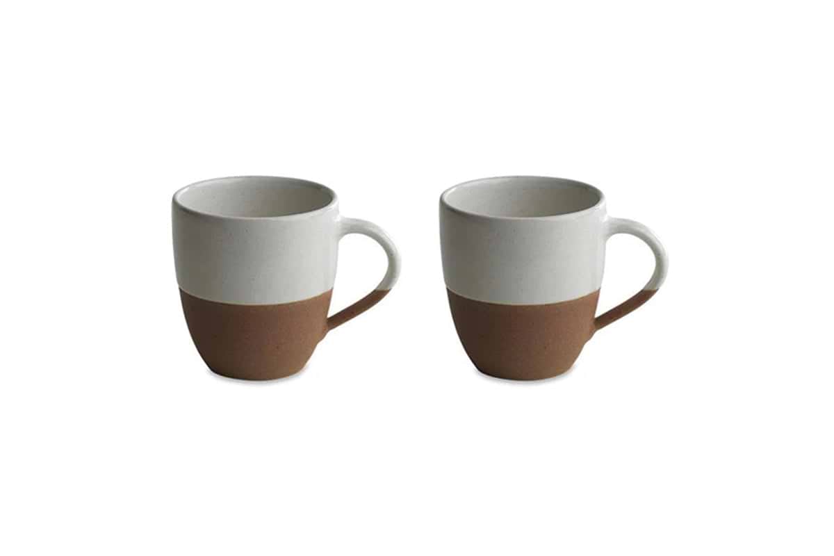 Two nkuku Mali White & Terracotta ceramic mugs with handles are shown side by side, each with an off-white glazed upper half and unglazed terracotta base, creating a minimalist two-tone look against a plain white background.