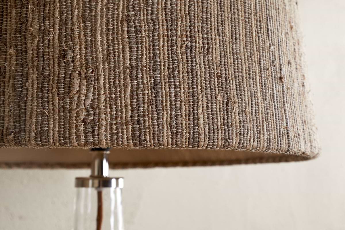 Close-up of the nkuku Nadee Banana Leaf Lampshade in Natural, featuring its textured, woven surface made from sustainable banana leaf fibers. Below, part of a clear glass base with a metallic fitting is visible.