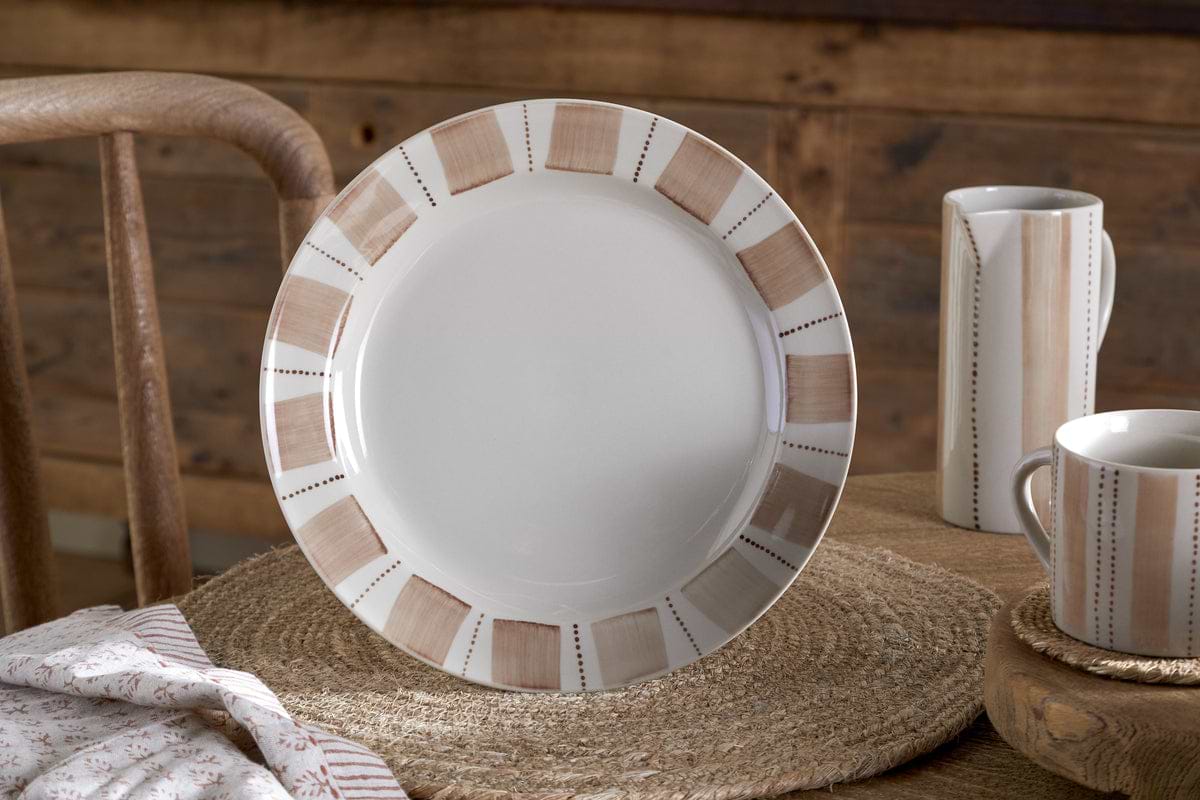 The Patthar Dinnerware Set by nkuku, featuring cream and clay tones with a beige and brown geometric border, adds rustic charm to your table. The 12-piece set sits atop a woven placemat, completed by matching mug and creamer.