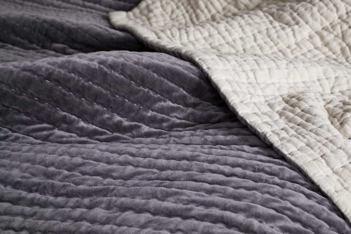 A close-up of the nkuku Nidra Velvet & Linen Bed Quilt - Charcoal, featuring soft gray cotton velvet on one side, cream linen on the reverse, and detailed Kantha stitching—ideal for King and Super King beds.