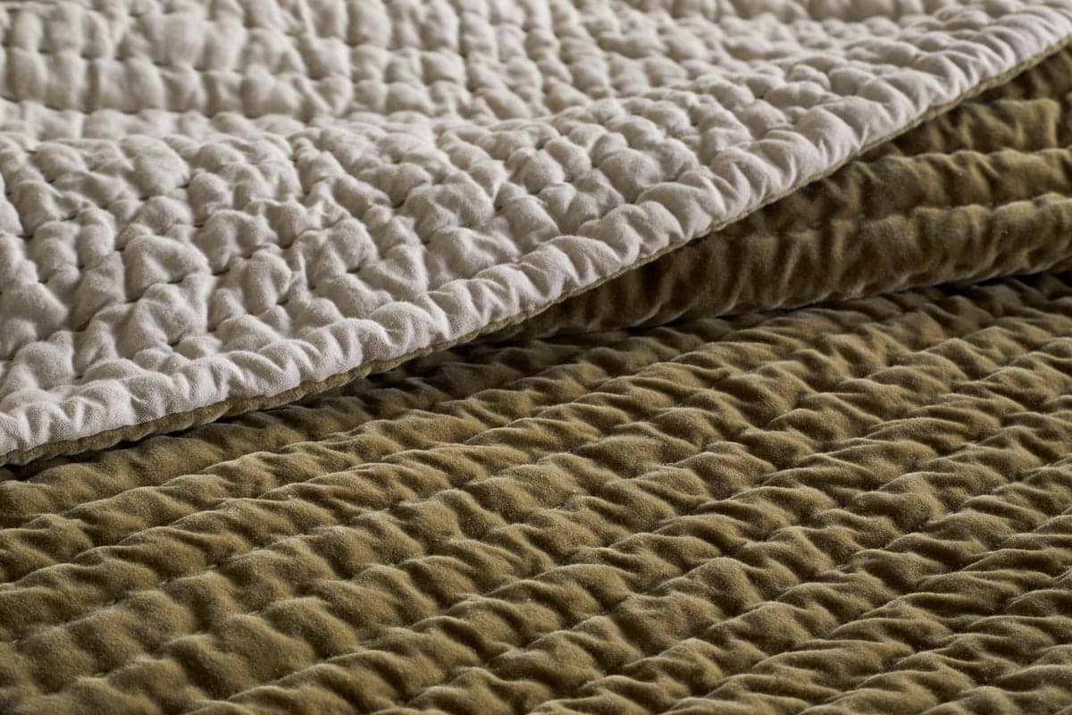 Close-up of two quilted layers—light cream and moss green—highlighting the soft, padded surface and stitched ridges of the nkuku Nidra Velvet & Linen Bed Quilt, crafted in cotton velvet style for king size bedding.