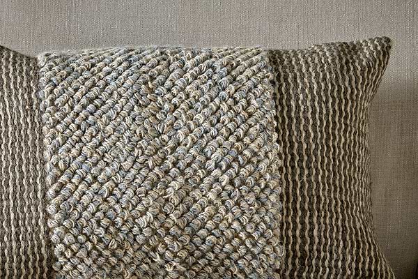 The nkuku Paduna Jute & Cotton Cushion Cover in Soft Blue & Brown features a textured, woven blend with a central braided panel and vertical stripes in beige and gray on a neutral background.