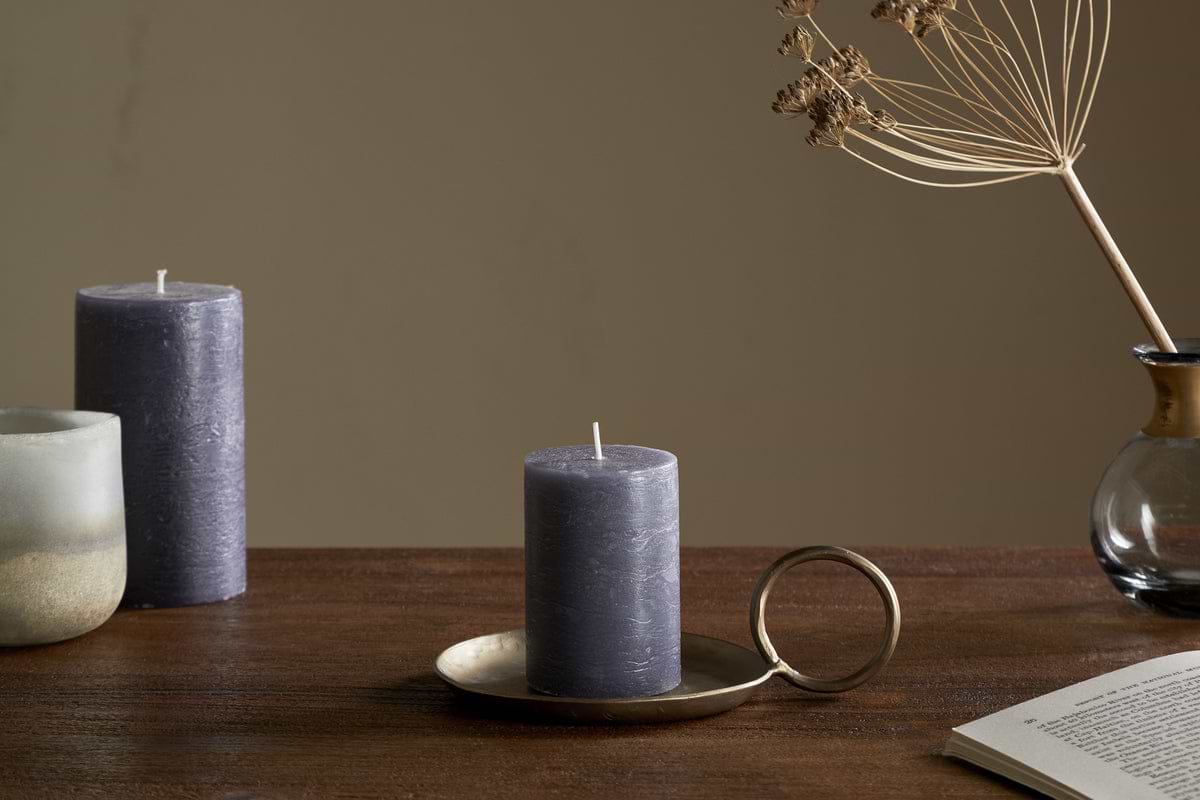 The nkuku Rustic Soy Blend Mini Pillar Candle in Charcoal, featuring a textured finish, sits on the table and adds a charming touch to the setting.