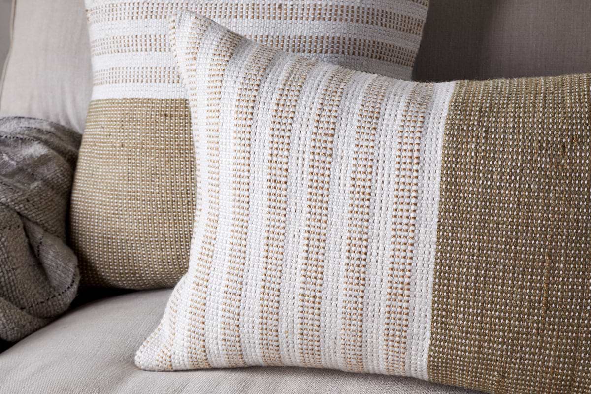 Two Samata Recycled Cushion Covers in Moss by nkuku rest on a light-colored couch. A gray knit throw blanket is partially visible on the left side.