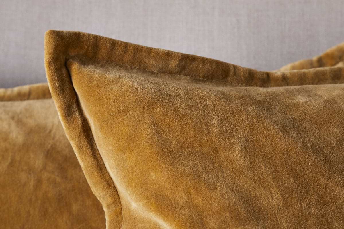 Close-up of the nkuku Sela Velvet Cushion Cover in ochre, featuring a plush texture and visible edge seam, set against a neutral gray background.
