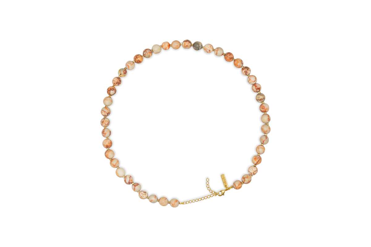 The Cerita Necklace - Rhodochrosite by nkuku features round, marbled beige and peach semi-precious stones with a gold chain extender and clasp, offering a versatile accessory.
