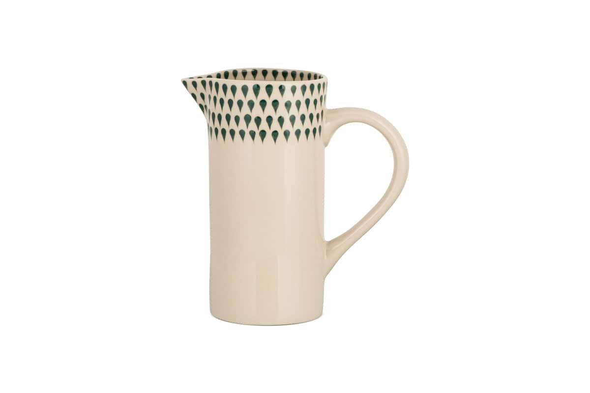 The Juniper Drop Jug - Cream & Juniper - Small by nkuku features a cream ceramic body, curved handle, and narrow spout. Its upper rim is adorned with dark green teardrop patterns—ideal for contemporary tableware collections.