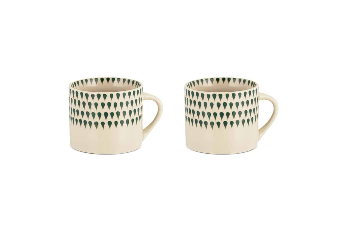 The nkuku Juniper Drop Mug - Cream & Juniper - Small (Set of 2) features two cream ceramic mugs with unique handles and juniper green drop details, displayed side by side on a white background.
