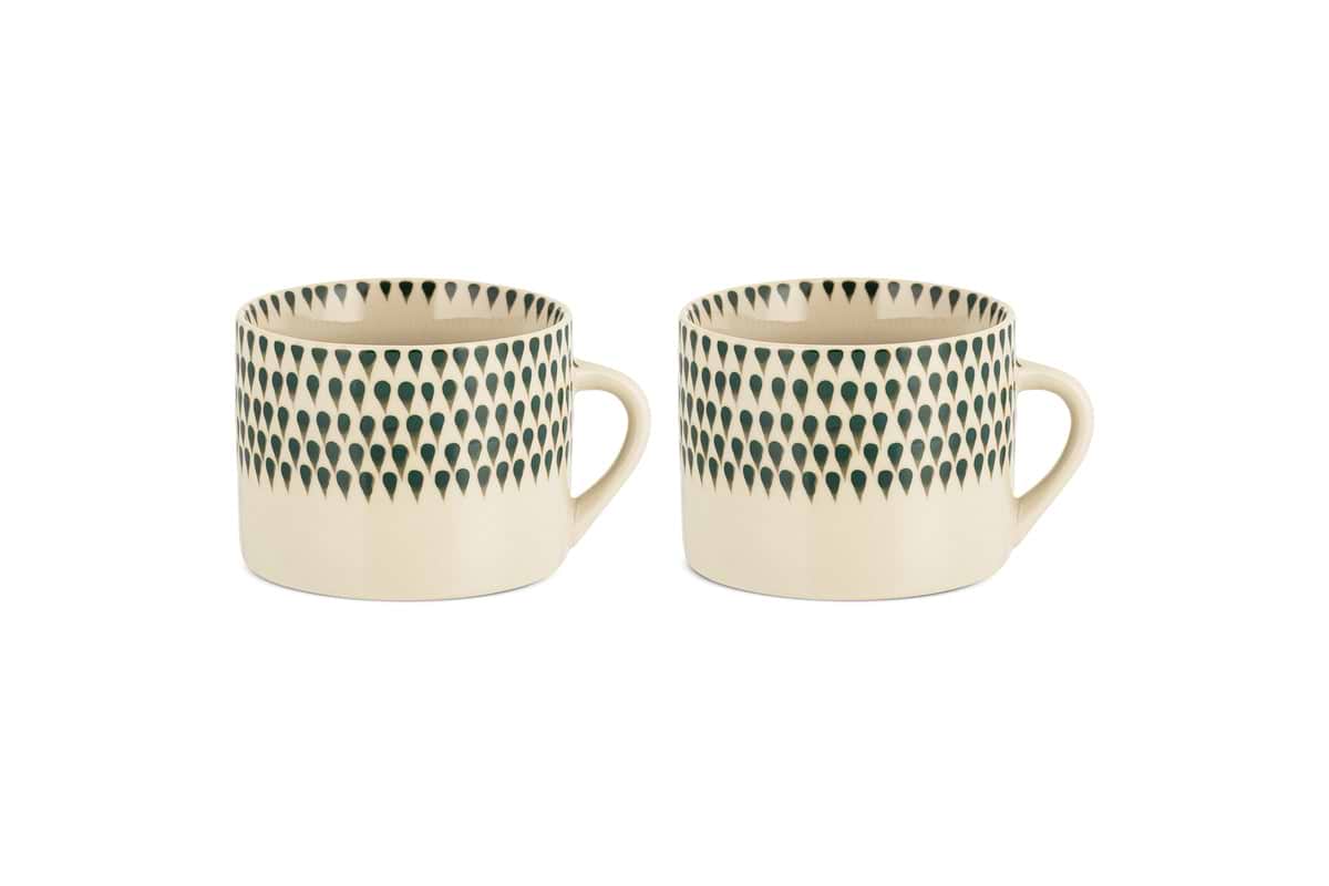 The nkuku Juniper Drop Mug - Cream & Juniper - Large (Set of 2) features two cream ceramic mugs with distinctive handles and a dark juniper green drop design near the rim, shown side by side on a white background.