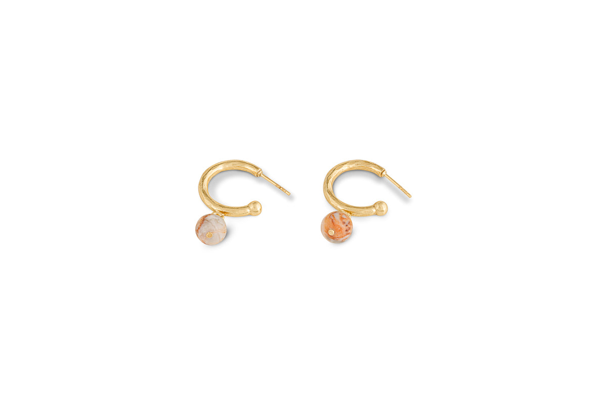 The Cerita Rhodochrosite Earrings by nkuku feature small gold-plated, textured hoops with round marbled orange and beige rhodochrosite charms. Suitable for pierced ears, they make a lovely jewellery gift. Shown on a plain white background.