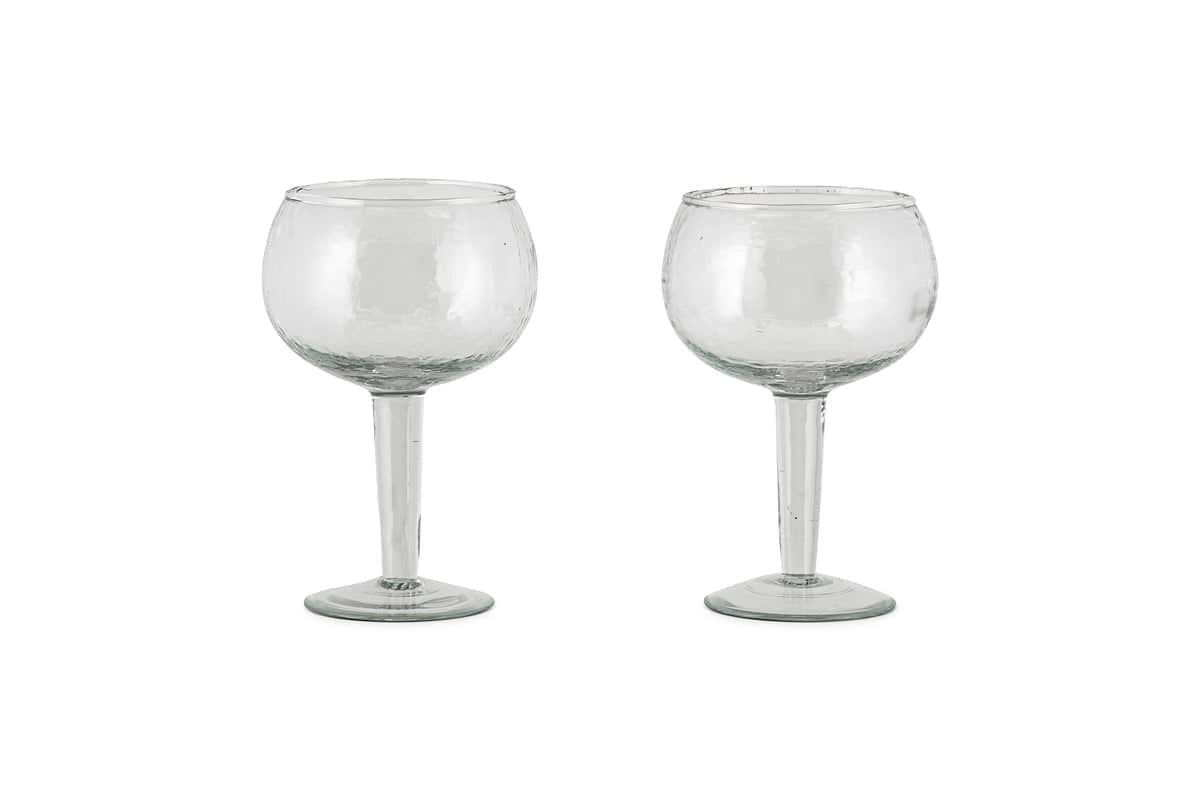 Two clear Yala Hammered Gin Glasses by nkuku, featuring round bowls and long stems, are displayed side by side on a white background. Set of 2.