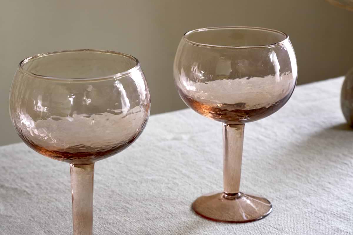 A set of two nkuku Yala Hammered Gin Glasses in Dusty Terracotta sits on a light tablecloth against a neutral background.