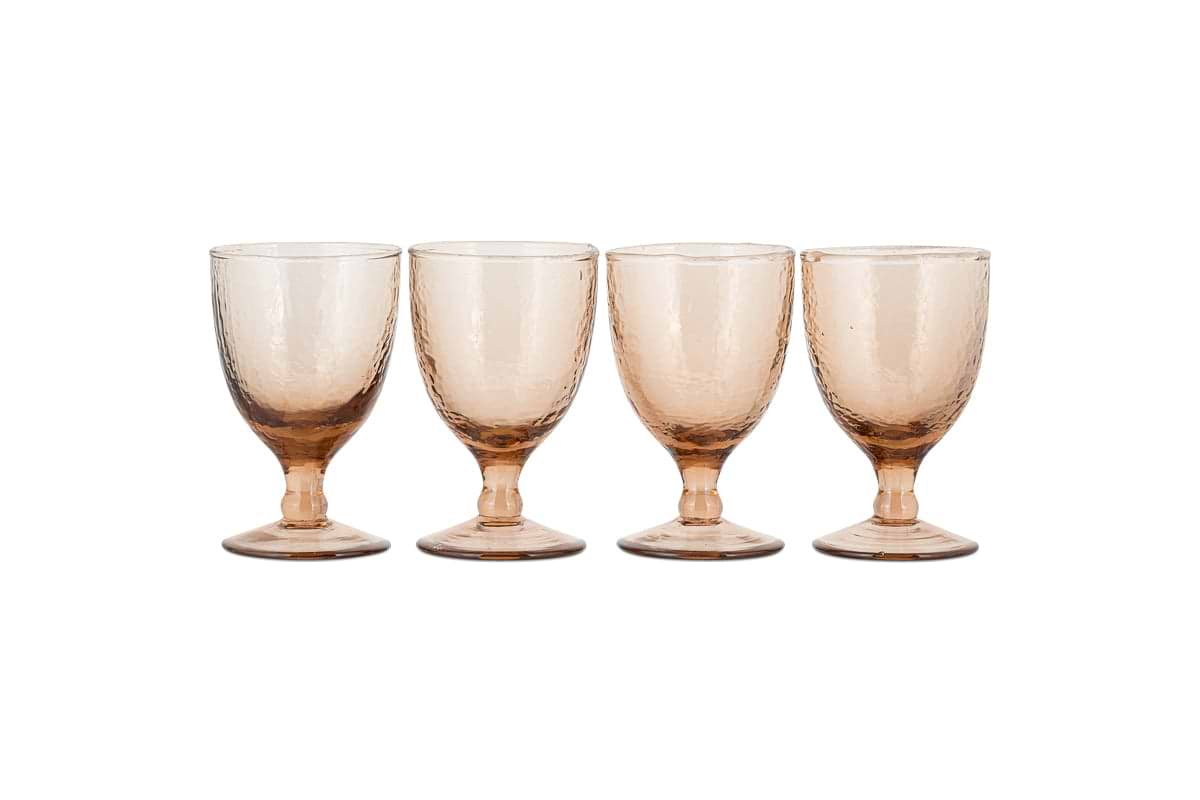 The nkuku Yala Hammered Wine Glass Set in Dusty Terracotta features four short-stemmed, amber-toned goblets with a subtle hammered pattern, round base, and slightly flared rim, arranged on a white background.