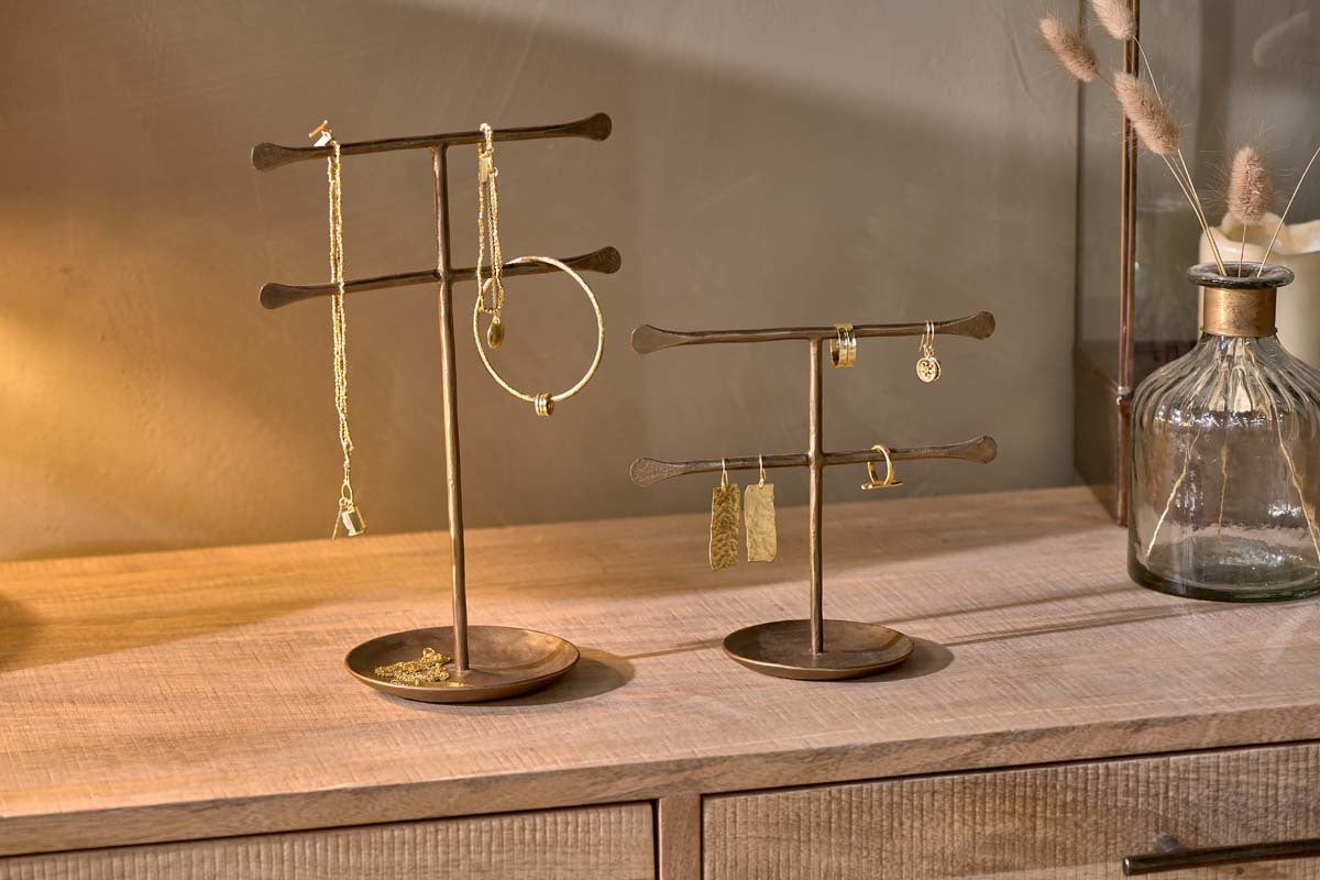 Two nkuku Liman Jewellery Stands with horizontal bars display gold jewellery on a light wooden dresser. Nearby, a glass vase with dried grasses sits against a beige wall, creating a warm, minimalist look.