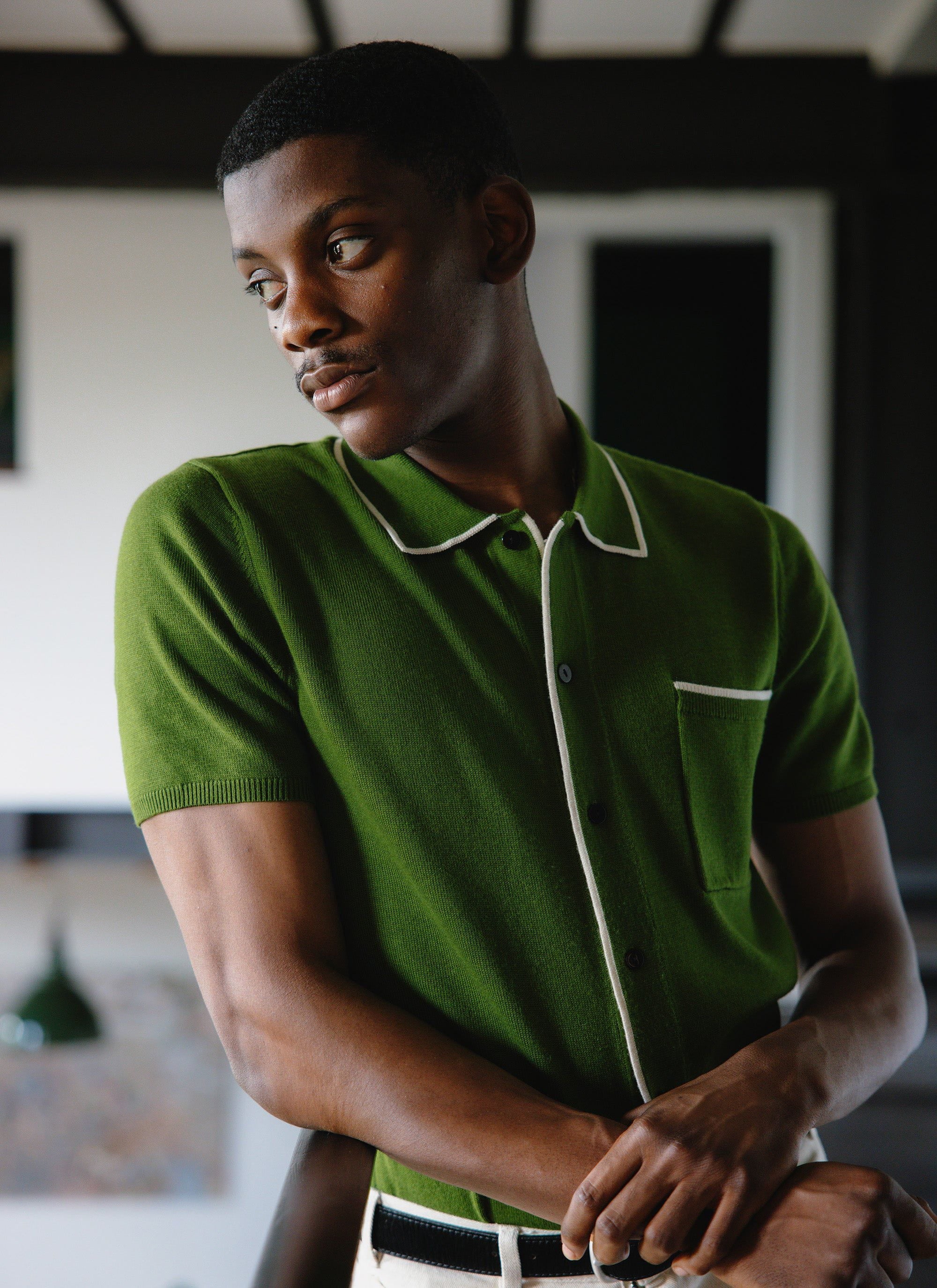 A model wears the Percival Contrast Trim Shirt in forest green, a wool-blend knit with ecru piping on the collar and pocket.