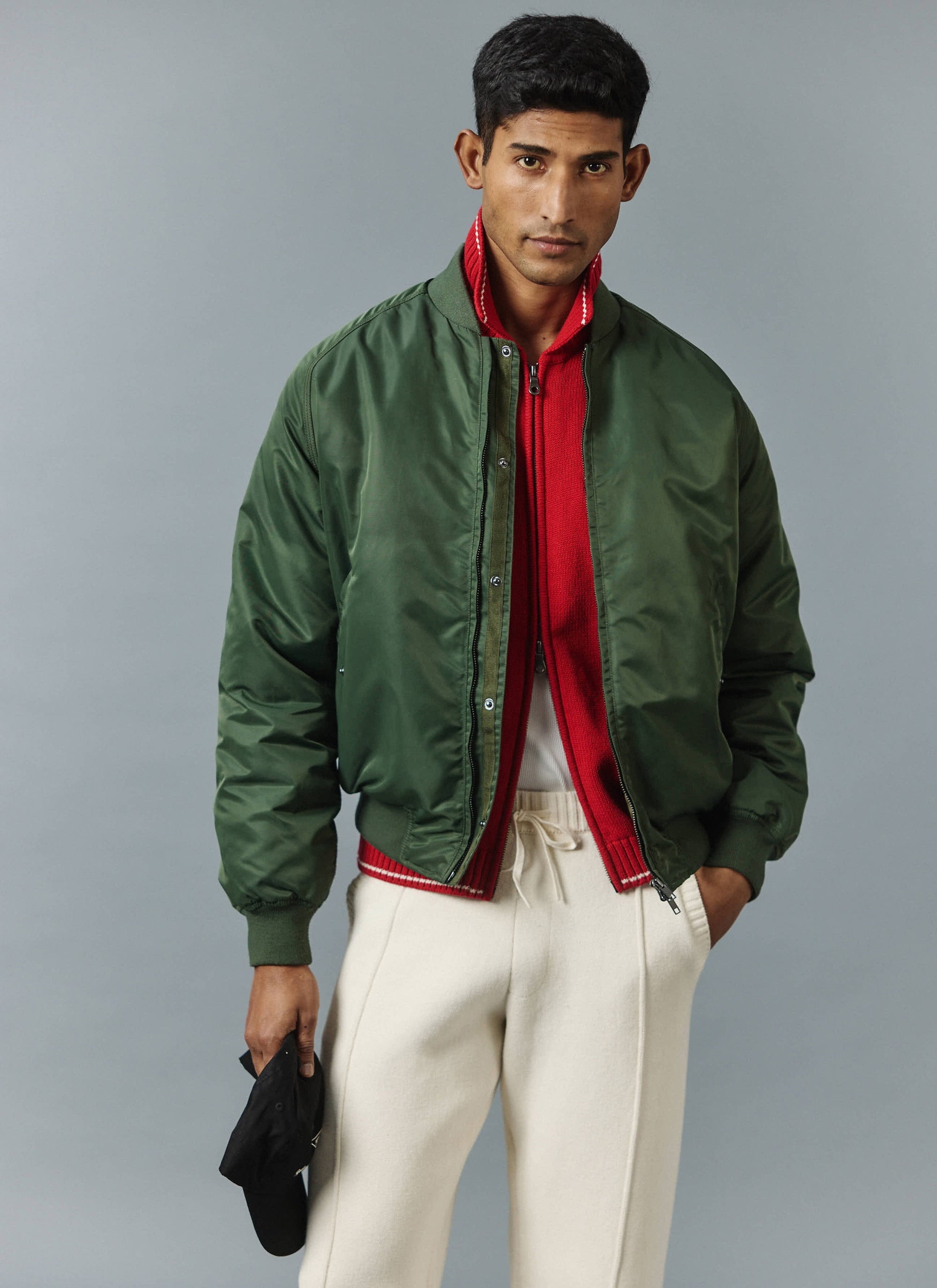 A model wears the Percival forest green nylon bomber jacket, layered over the red Gardner knitted zip cardigan.