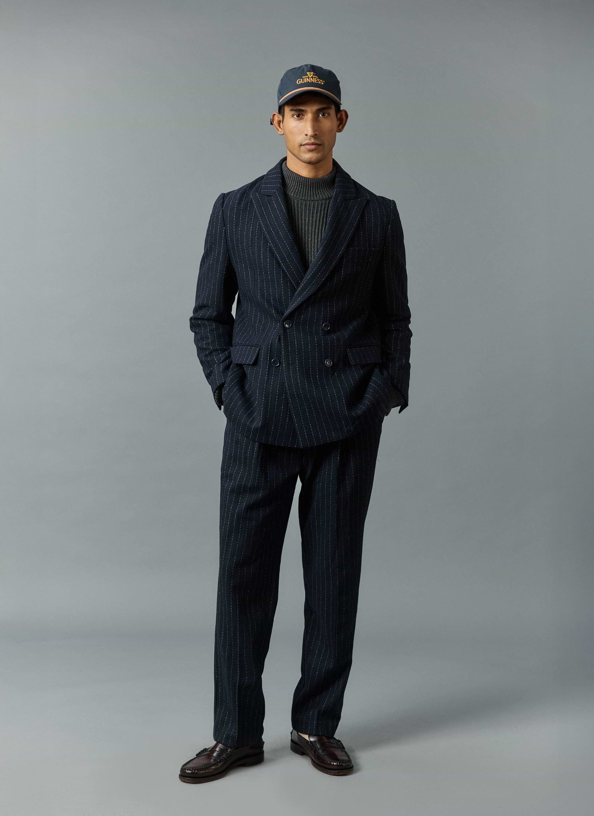 A model wears the Percival navy Textured Stripe suit, styled casually with a grey roll neck and a baseball cap.