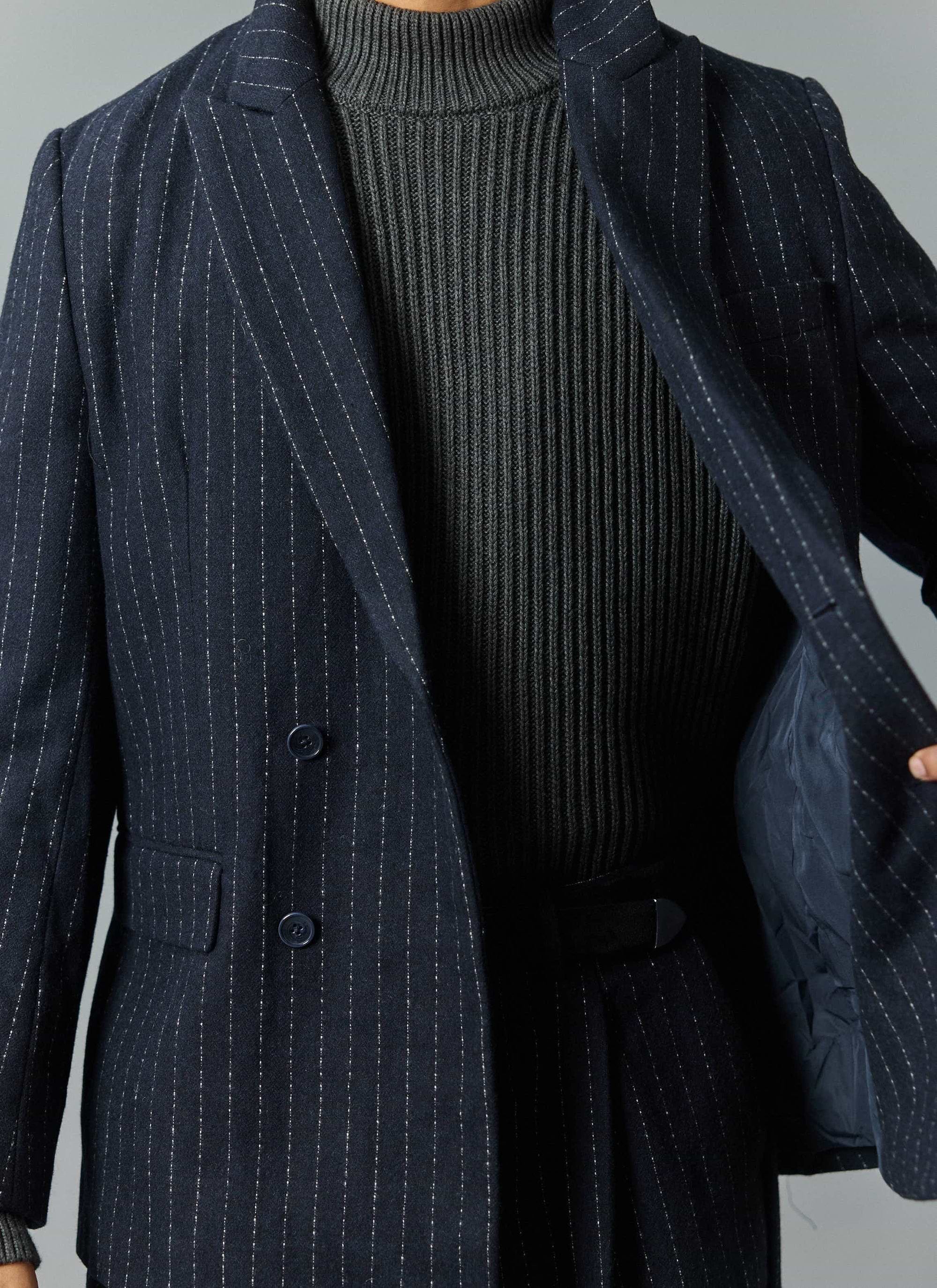 A close-up of a model wearing the navy Textured Stripe Double Breasted Blazer from Percival, over a grey ribbed jumper.