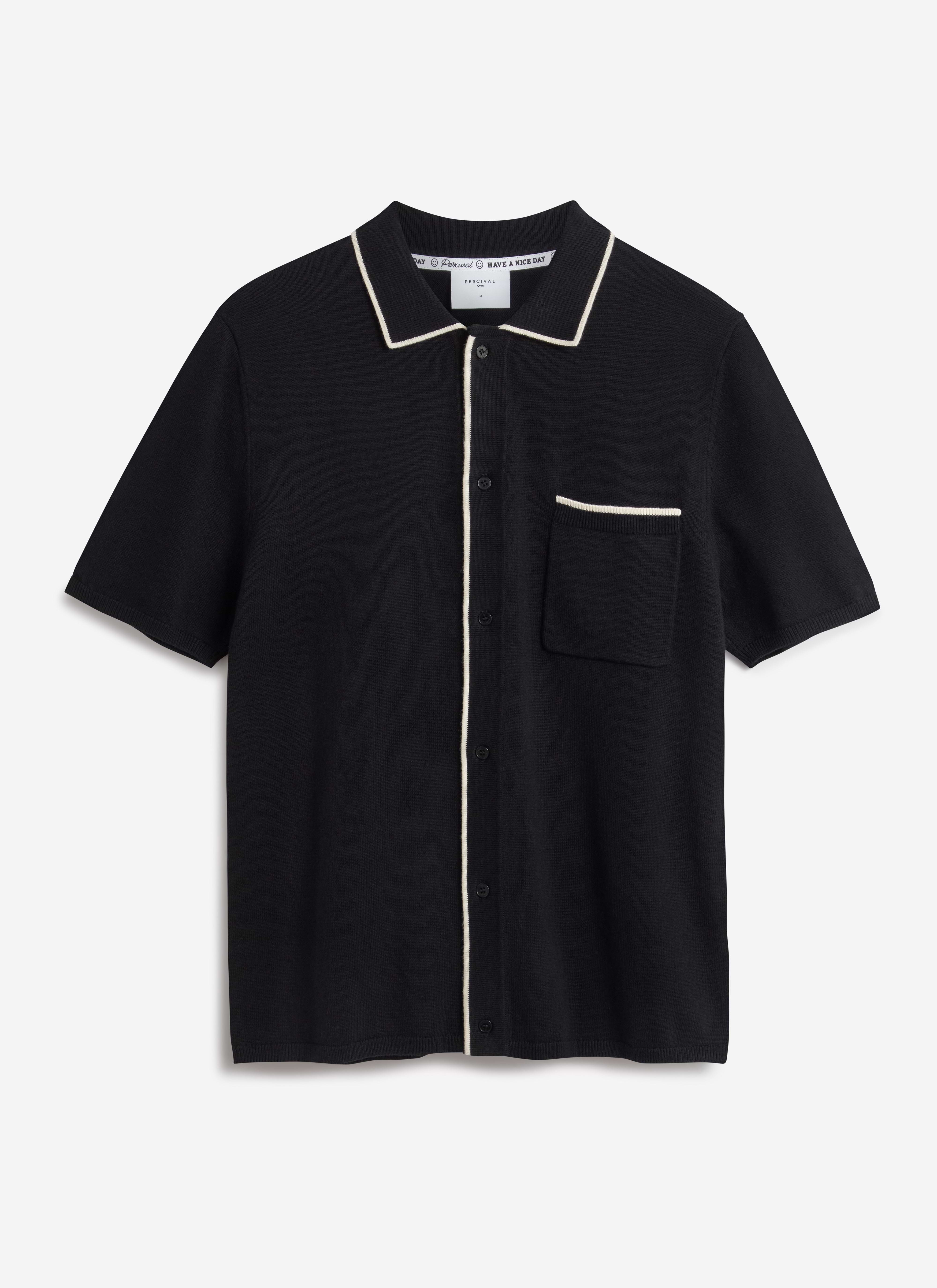A flat lay image of the Percival Contrast Trim Knitted Shirt in black, highlighting the ecru trim on the collar and pocket.