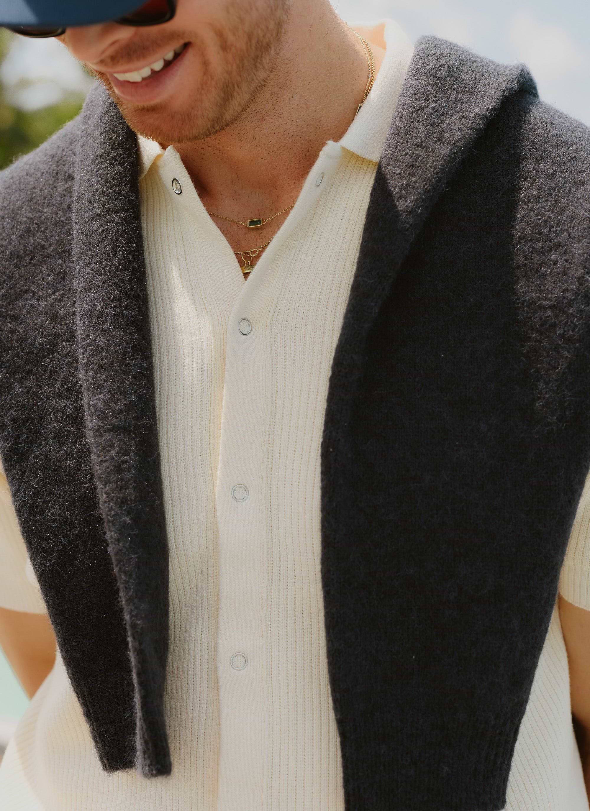 A close-up of a man wearing the cream Percival Pablo Cuban knitted shirt, styled with a dark jumper over his shoulders.