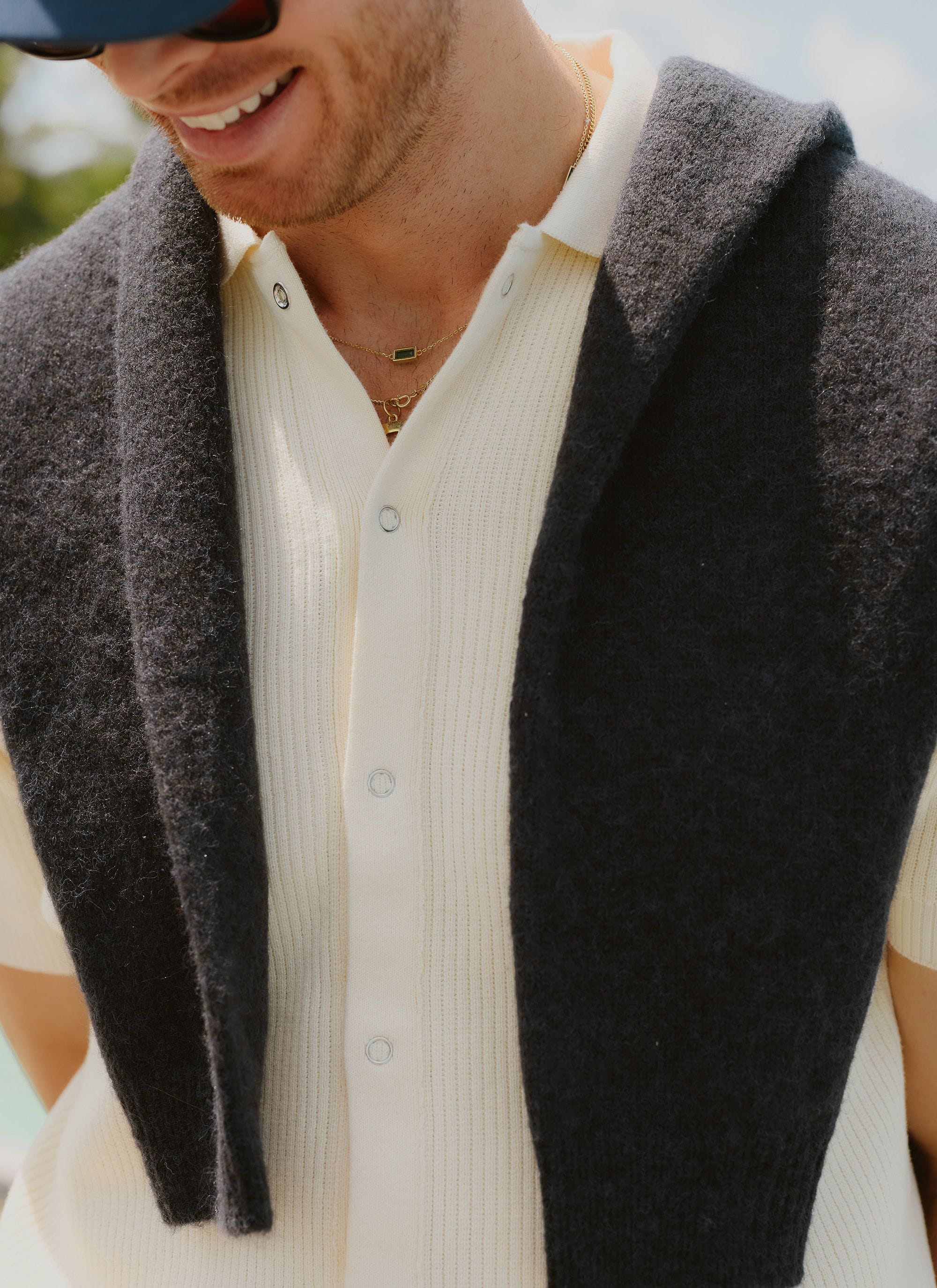 A close-up of a man wearing the cream Percival Pablo Cuban knitted shirt, styled with a dark jumper over his shoulders.