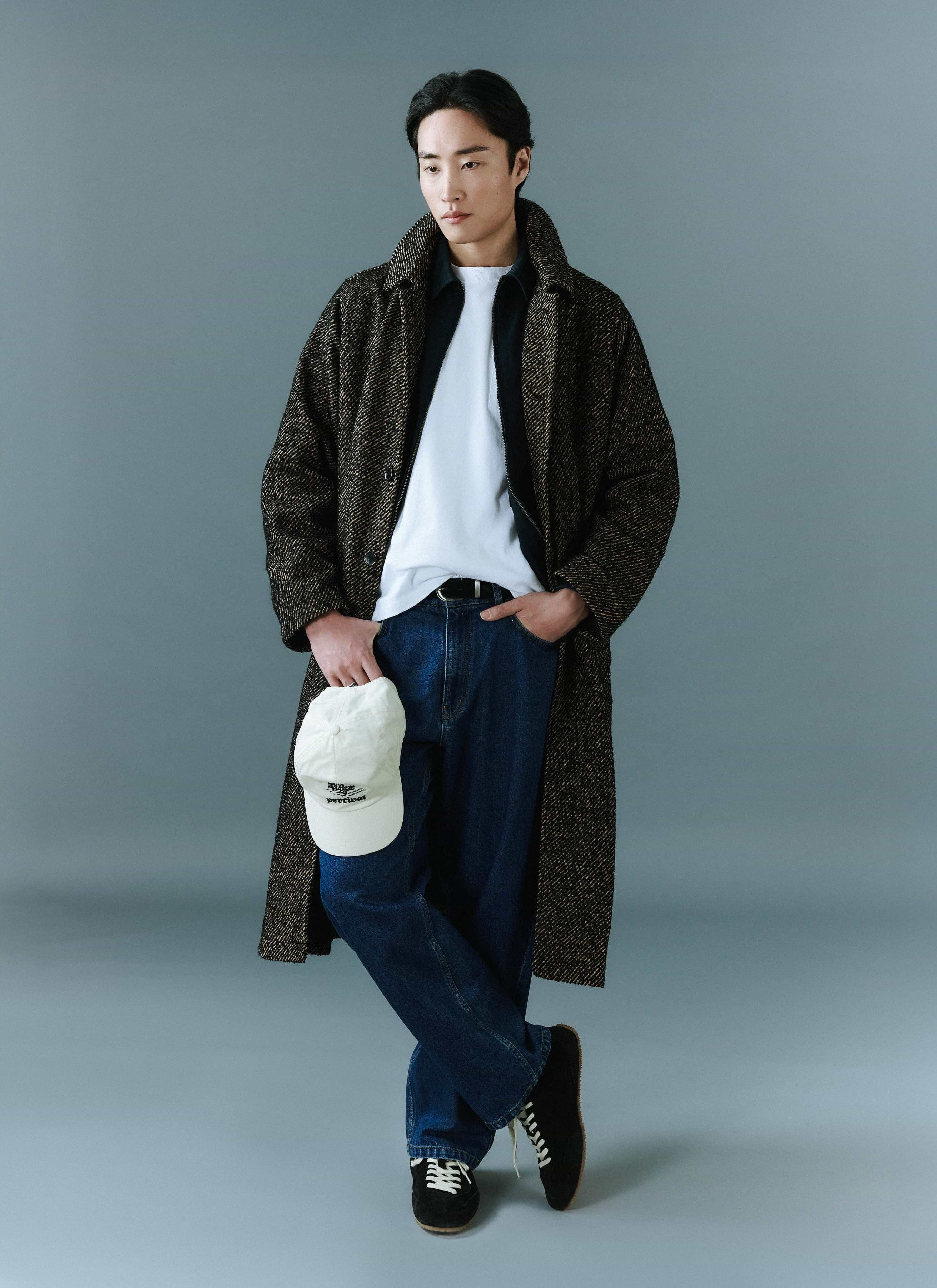 a model wears the percival menswear minnesota overcoat in oak herringbone twill with dark jeans and trainers.