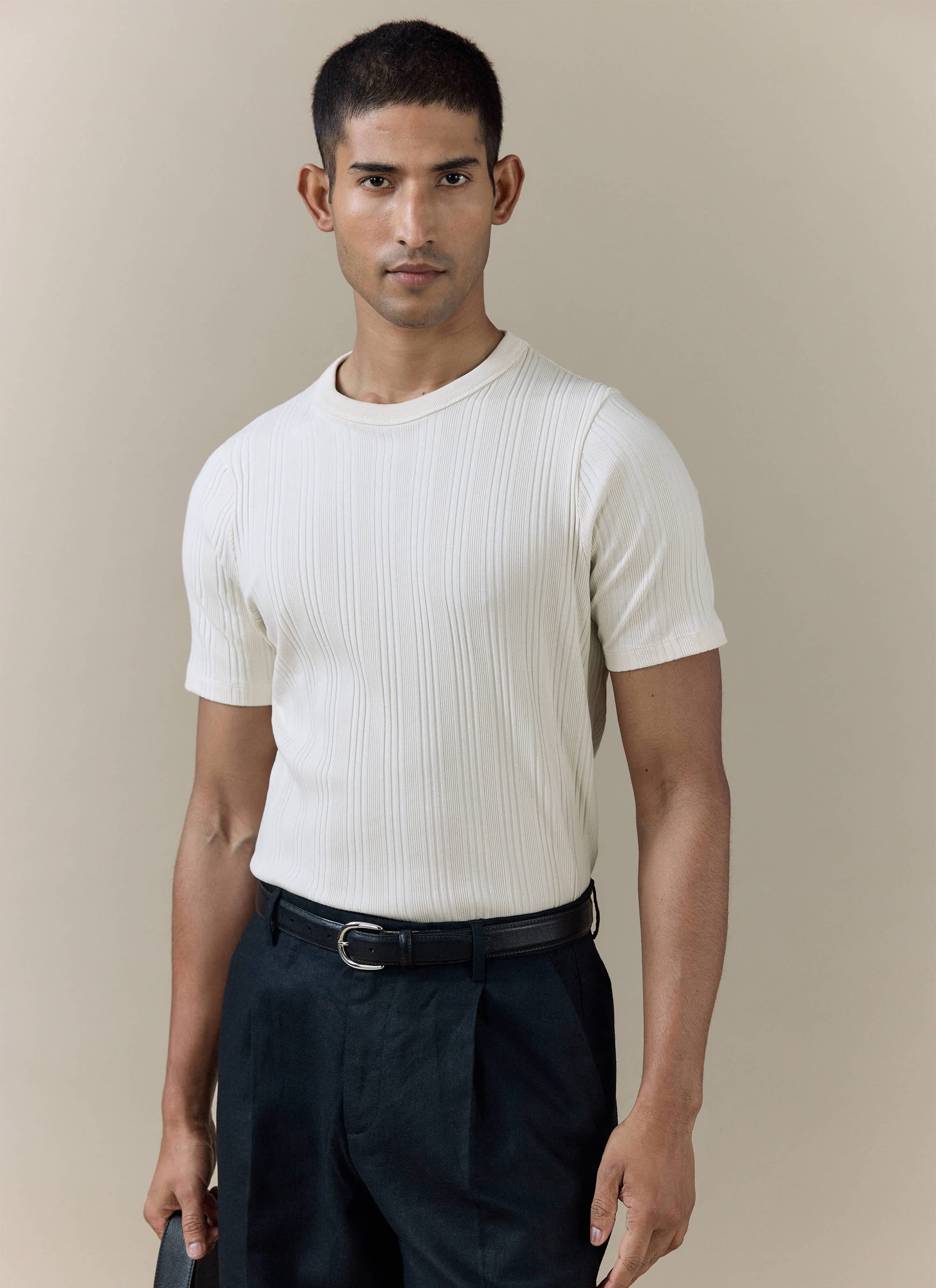 A model wearing the cream Percival Leon Ribbed T Shirt in organic cotton, featuring a textured vertical rib design.