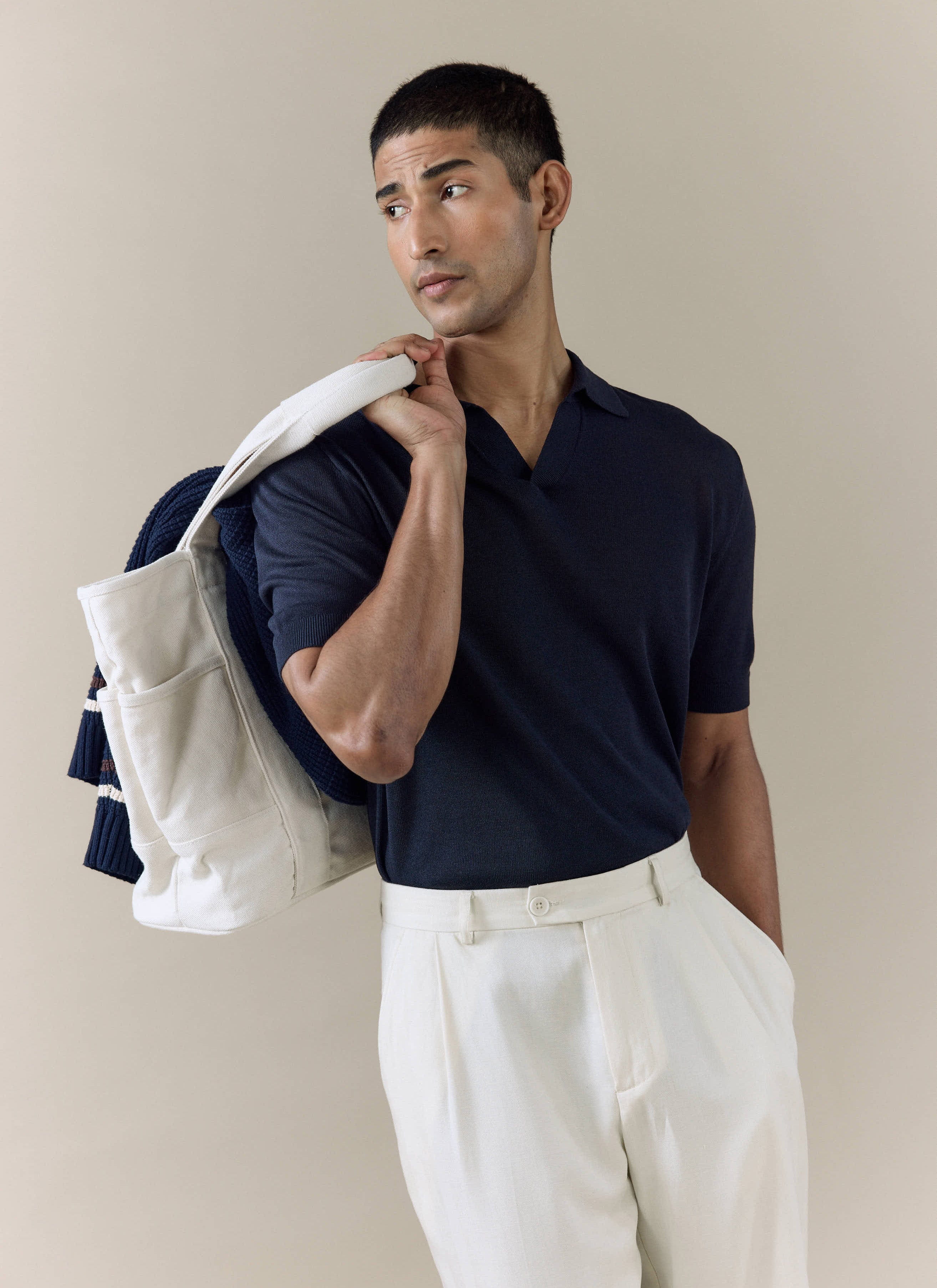 Model wearing the navy Percival Laurence Knitted Polo in a linen-lyocell blend, paired with cream pleated trousers.