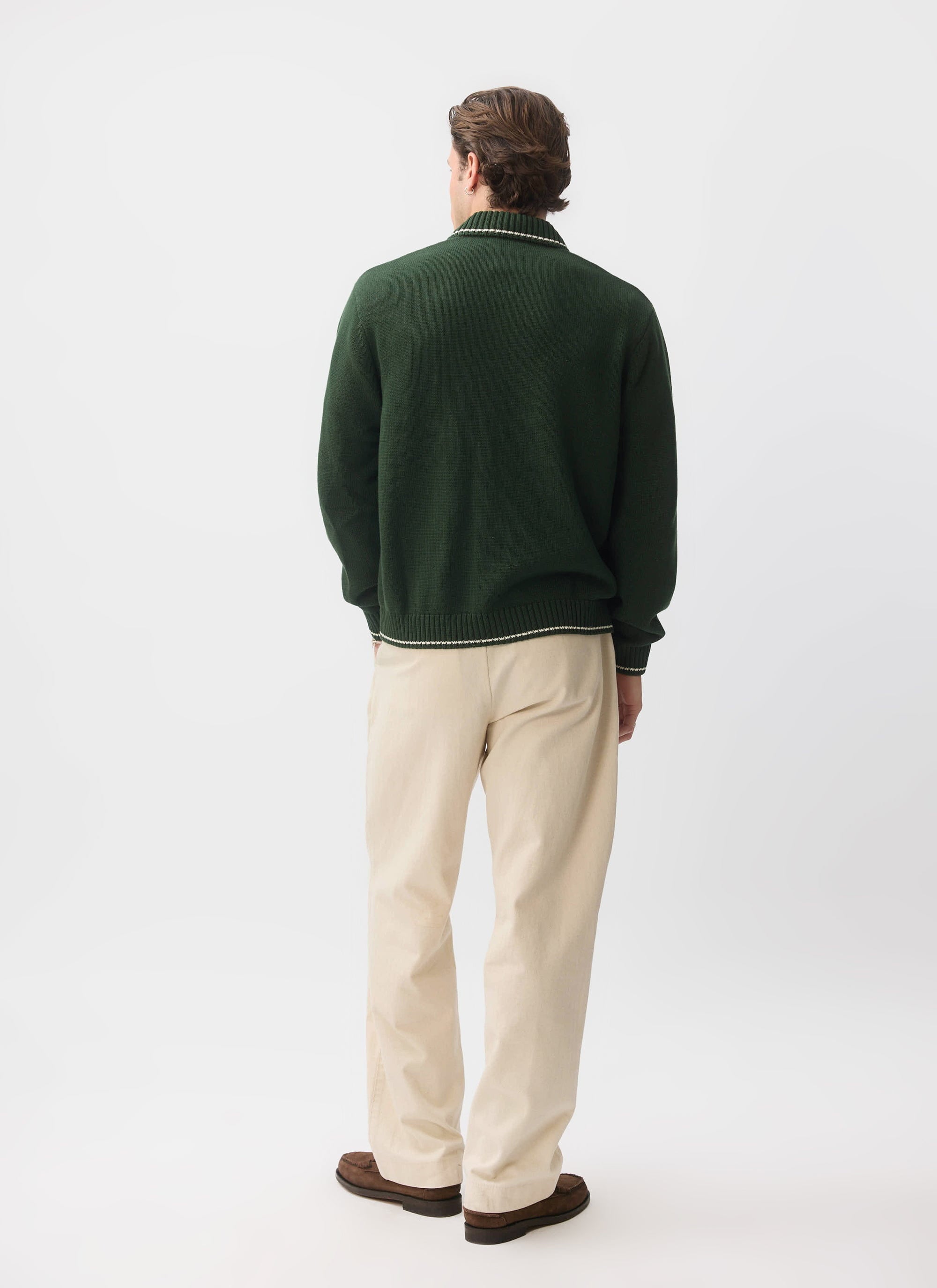 Back view of a model in the Percival Gardner Dense Knitted Zip Cardigan in forest green, styled with cream trousers.