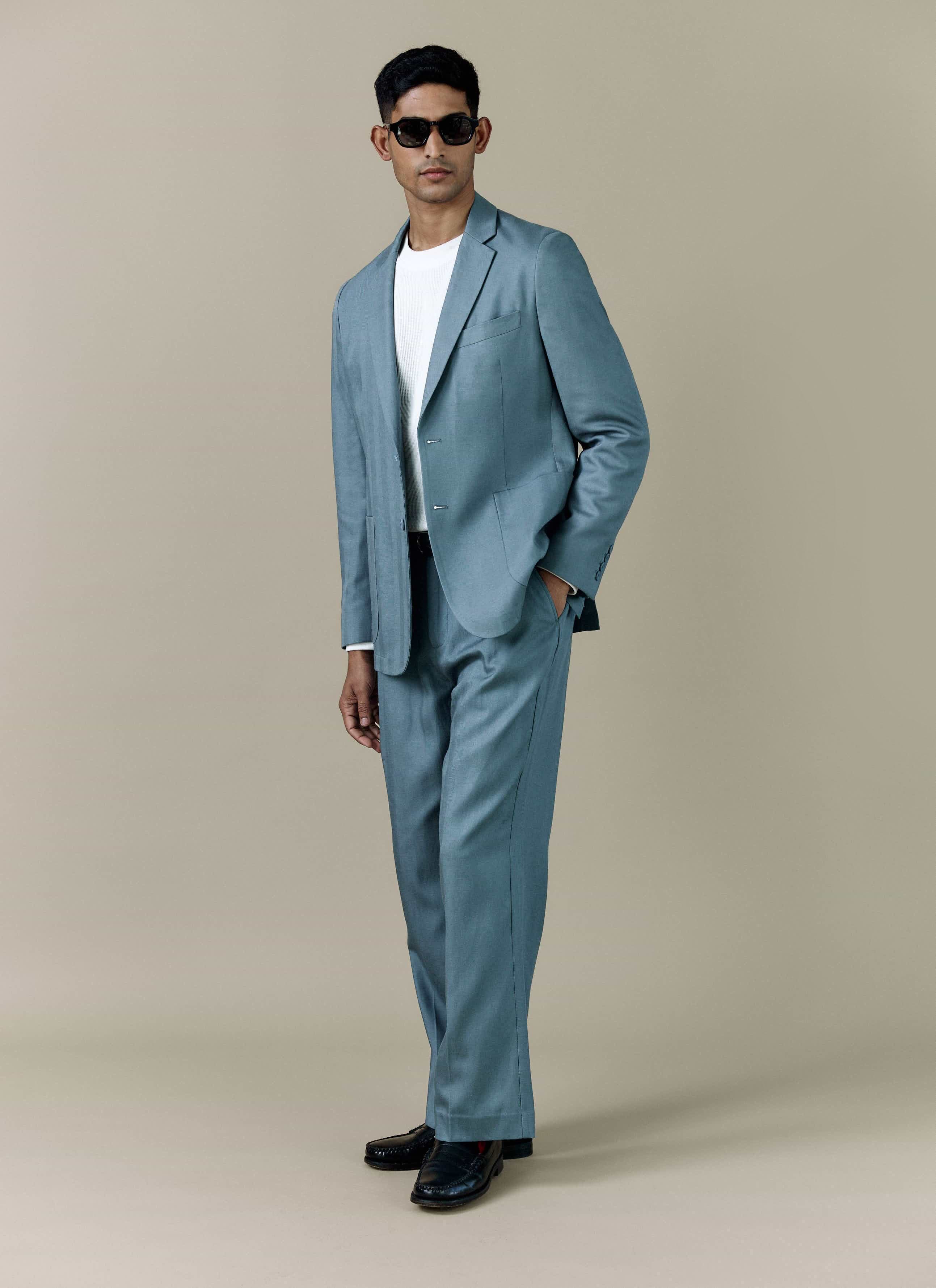 A model wears the Percival Lyocell Regular Blazer in Slate Blue, styled as a full suit with a white t-shirt and sunglasses.