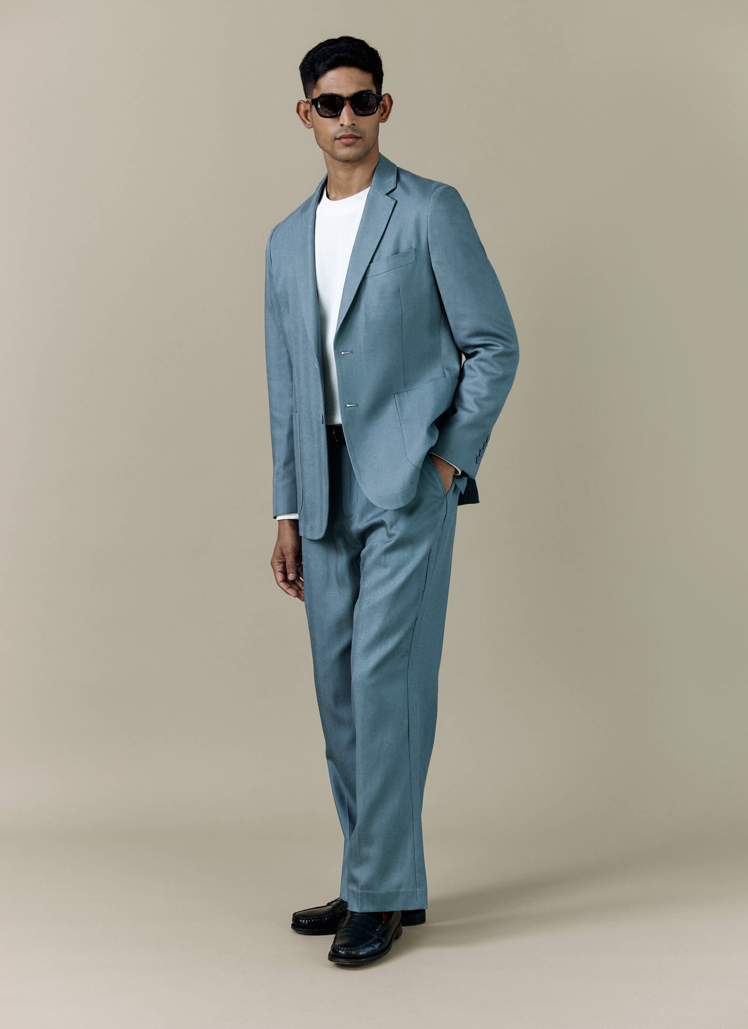 A model wears the Percival Lyocell Regular Blazer in Slate Blue, styled as a full suit with a white t-shirt and sunglasses.