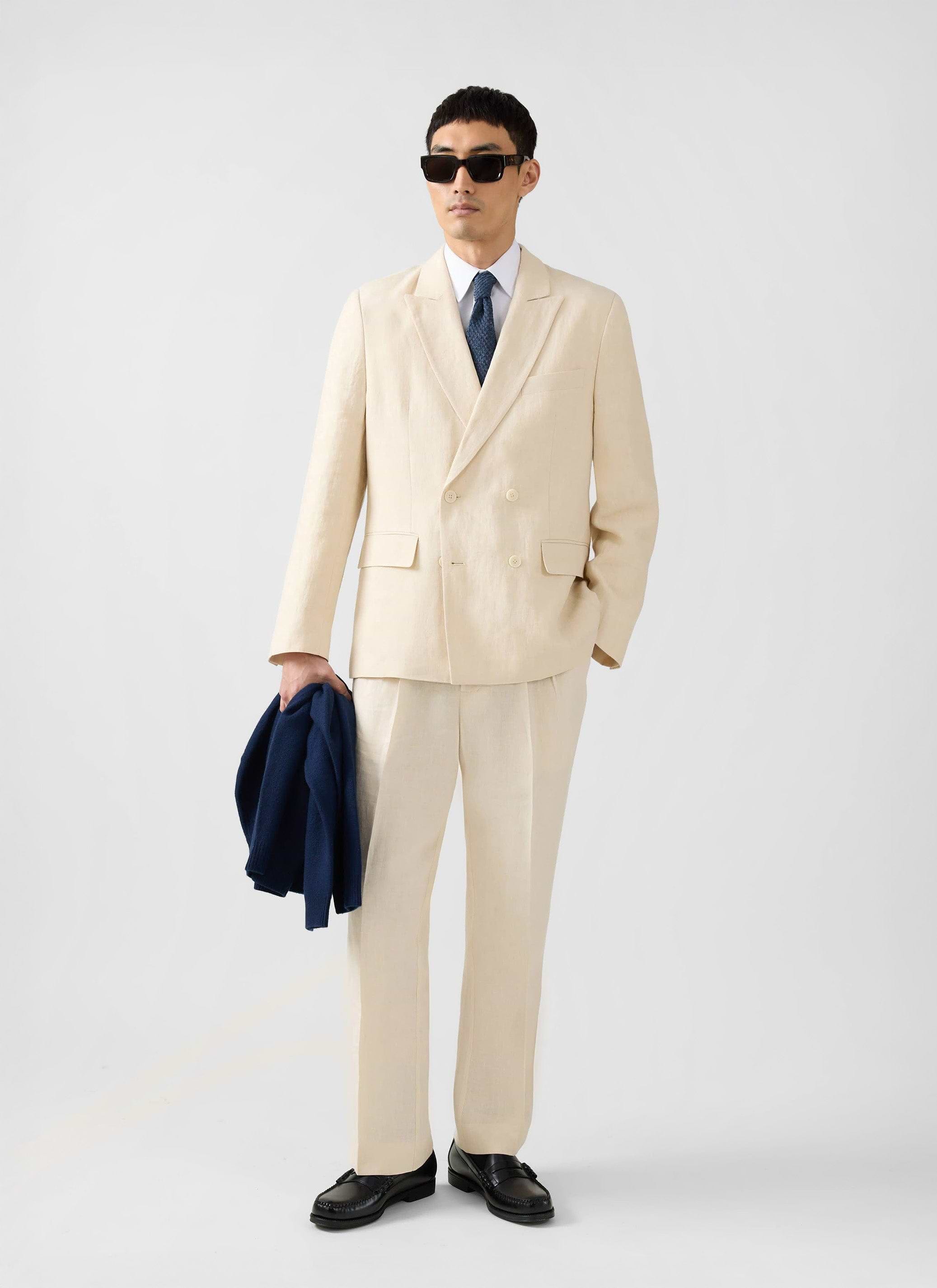 A model wears the full Percival Clifton suit in cream linen, featuring the double-breasted blazer, styled with sunglasses.