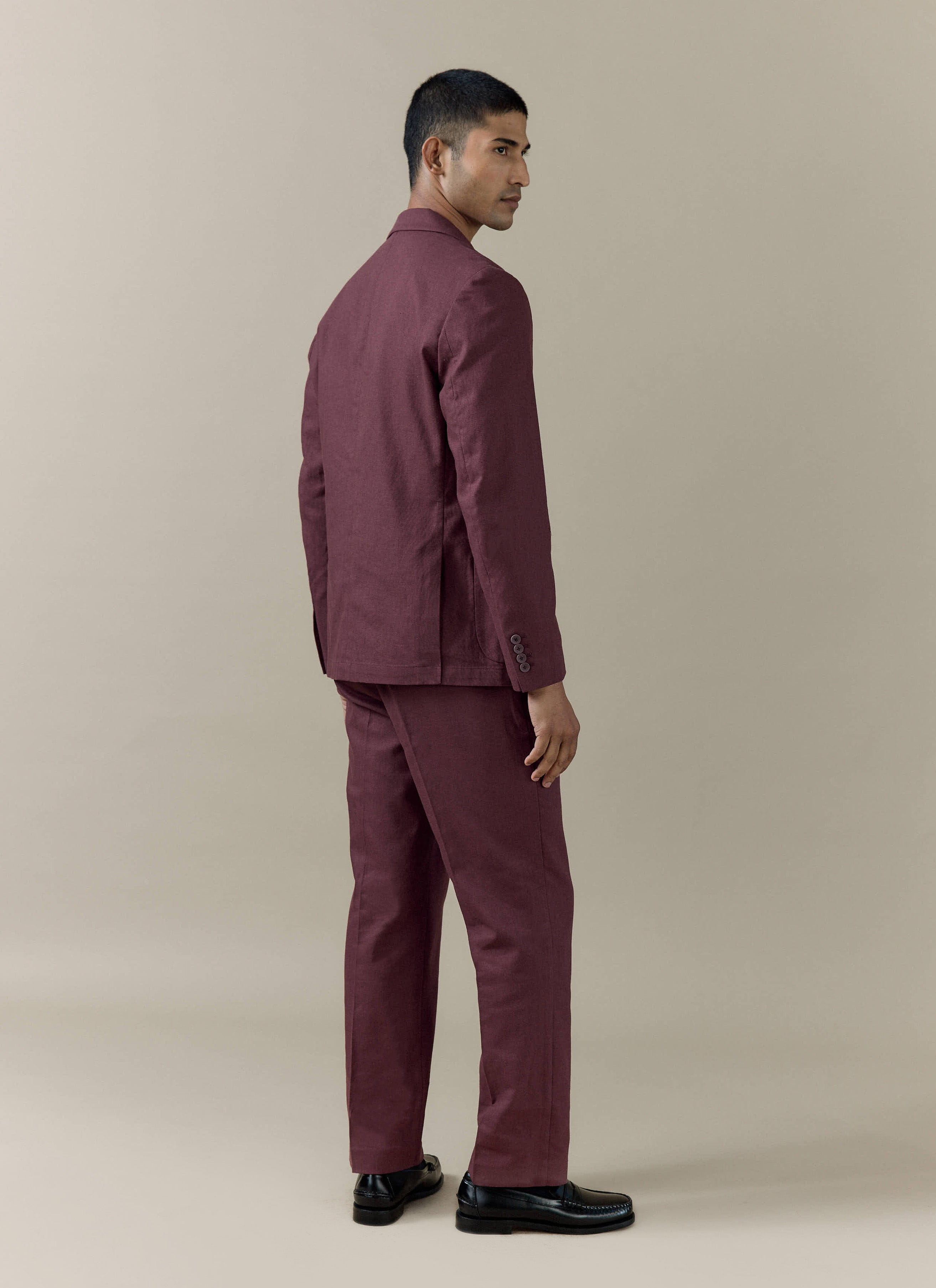 Tailored linen blazer and matching trousers in merlot by Percival, shown from a rear side-profile on a model.