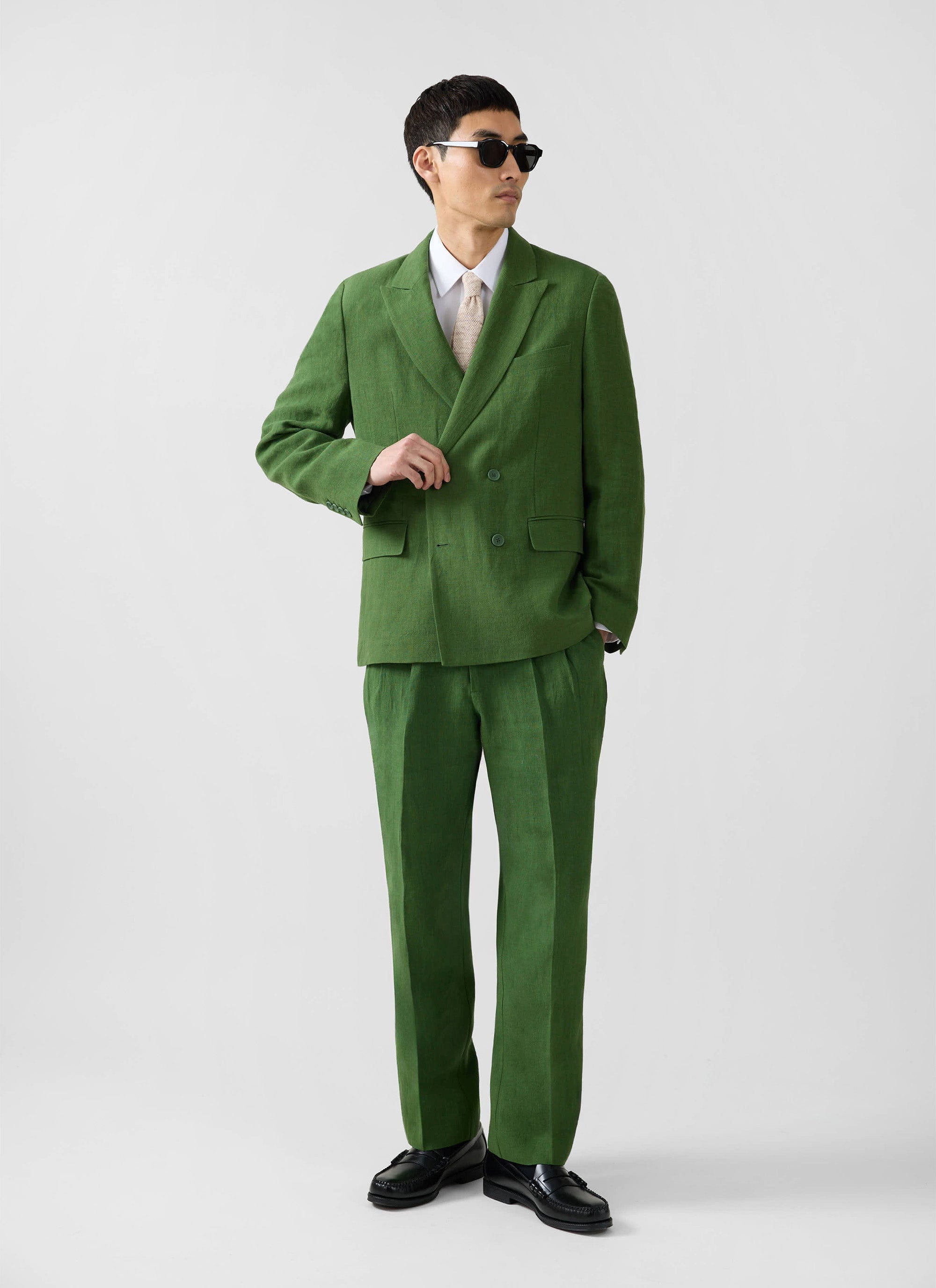 A man models the Percival Clifton Double Breasted Blazer and trousers in forest green linen against a studio background.