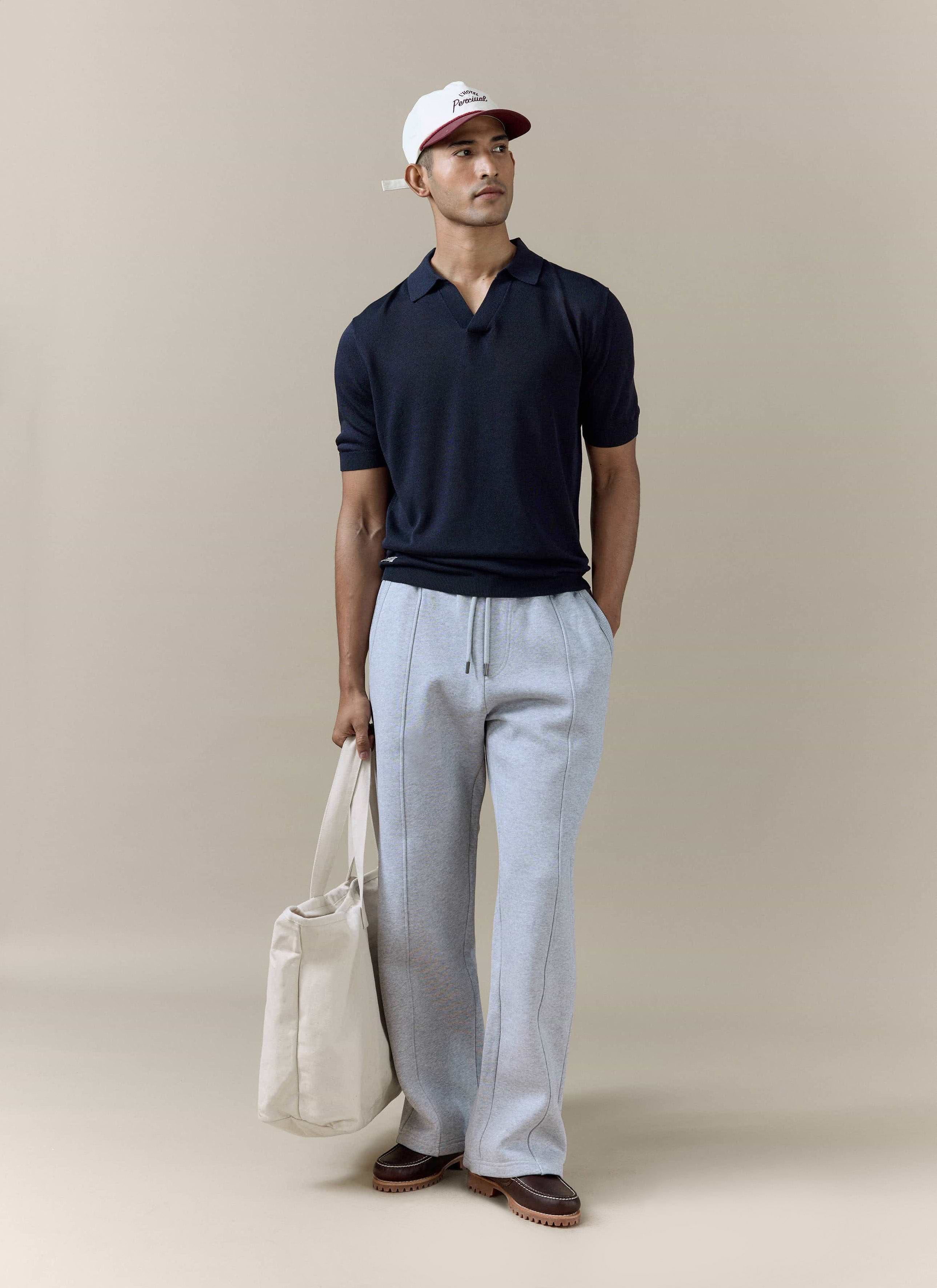 Navy Laurence Knitted Polo by Percival in a linen-lyocell blend, worn by a model with grey trousers and a cap.