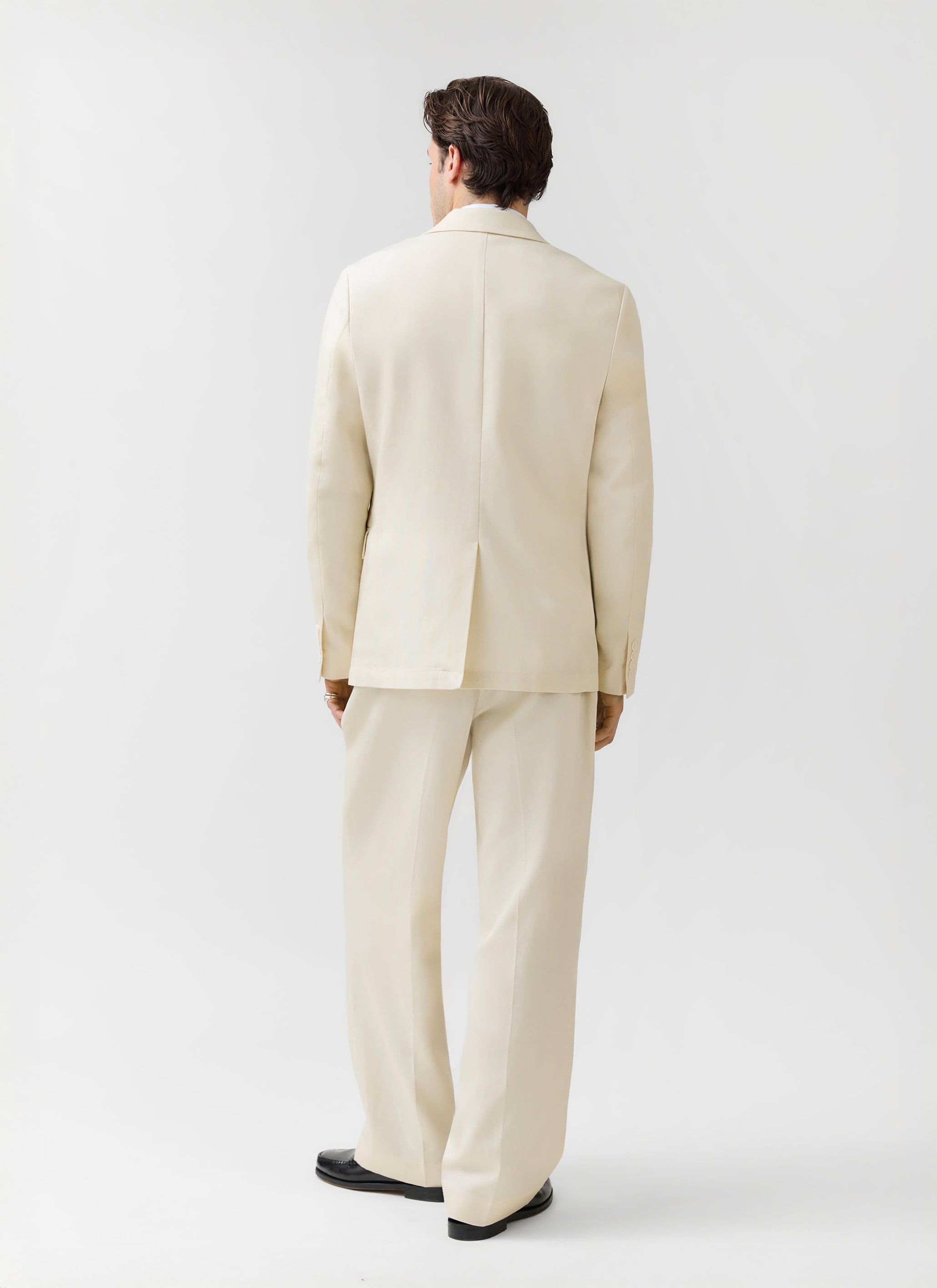 A model, seen from behind, wearing the Clifton 3 Button Blazer and matching suit trousers in cream from Percival.