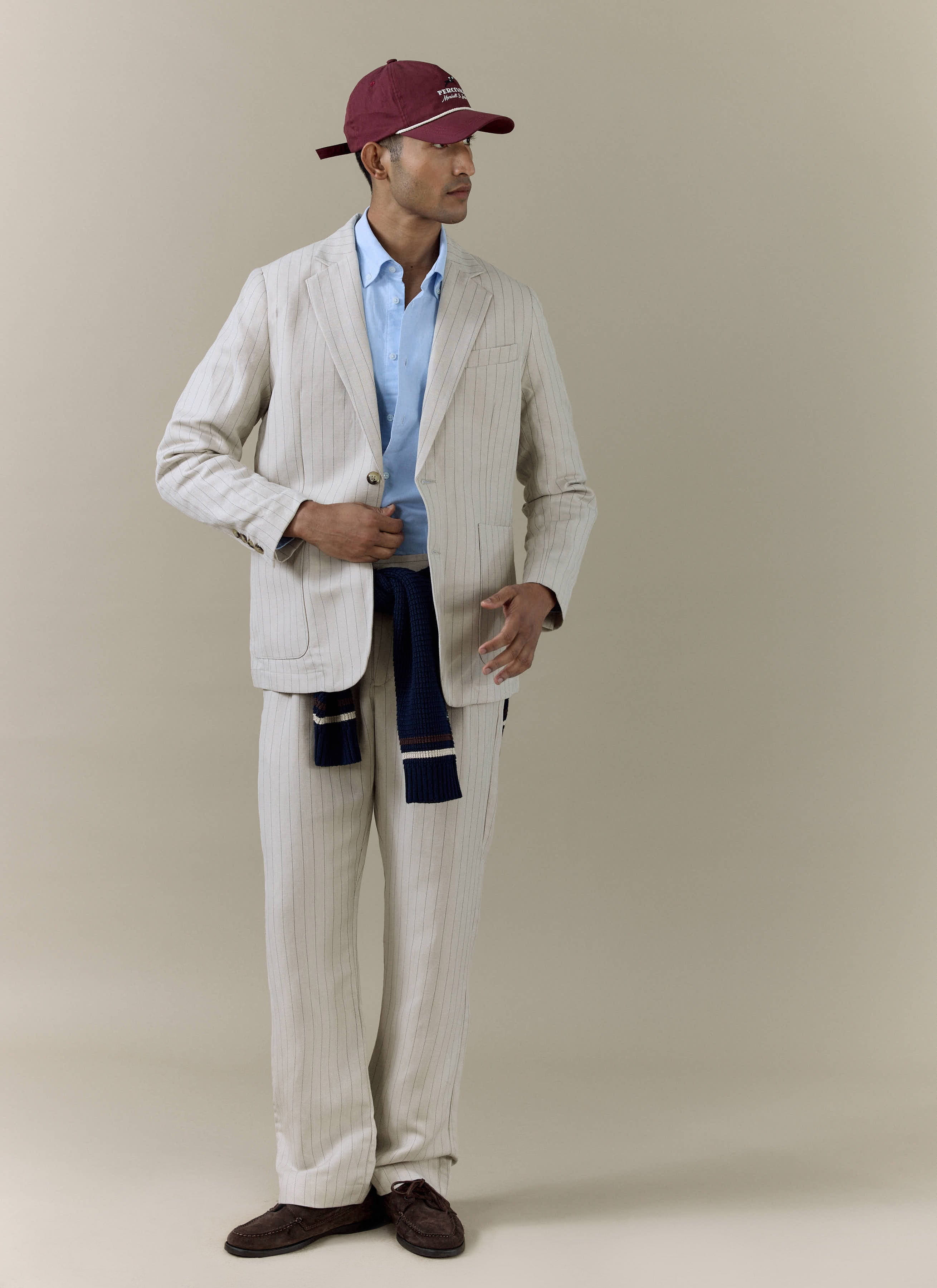 Percival cream striped linen blend blazer and matching trousers, styled with a light blue shirt and burgundy cap.