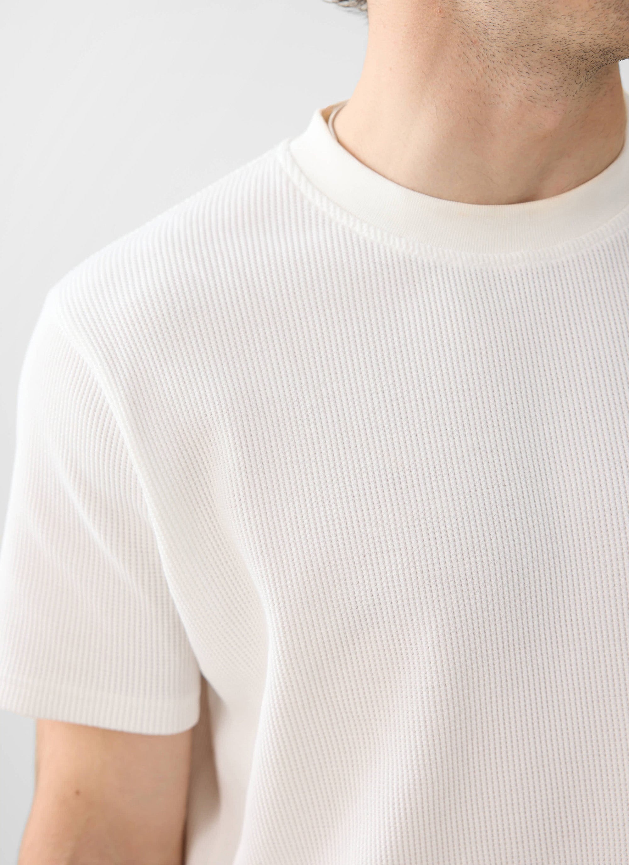 A close-up of a model wearing the white Waffle T-Shirt from Percival, highlighting the textured organic cotton knit.