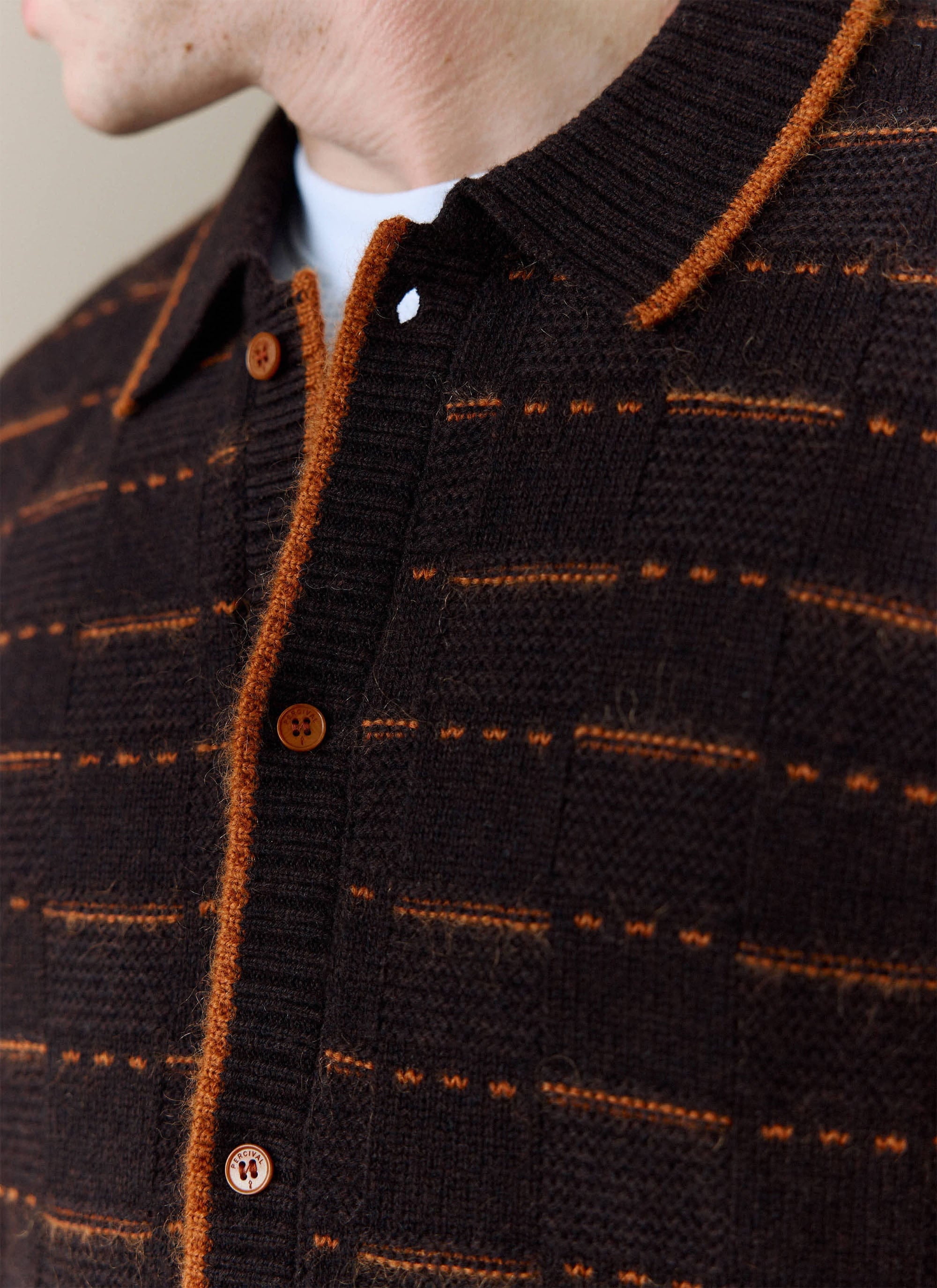 Close-up of a model wearing the brown Addison Knitted Shirt from Percival, showing the orange stitching and branded buttons.