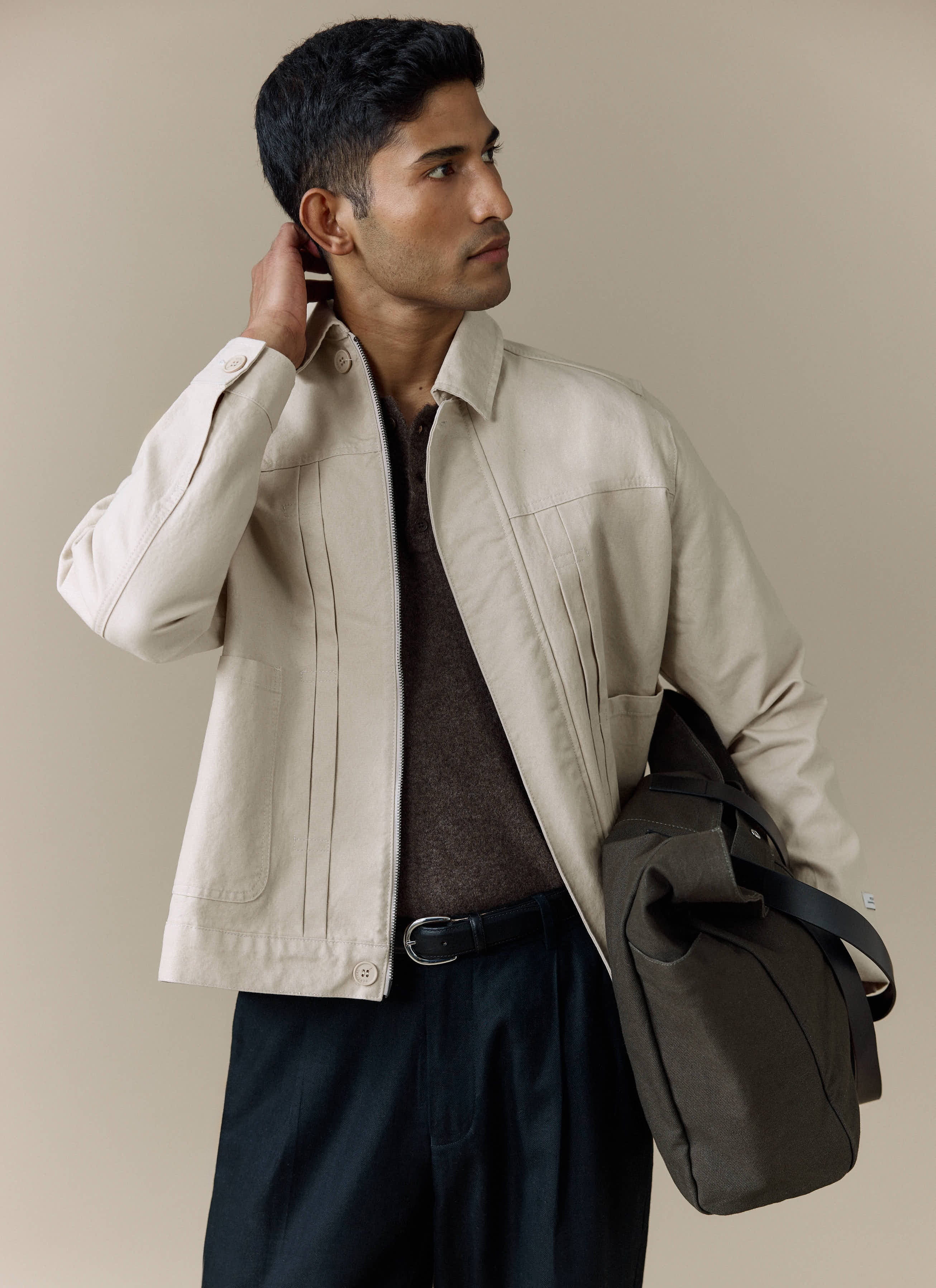 A model wears the Percival Ernst Jacket in ecru cotton, layered over a brown knit top and styled with dark trousers.