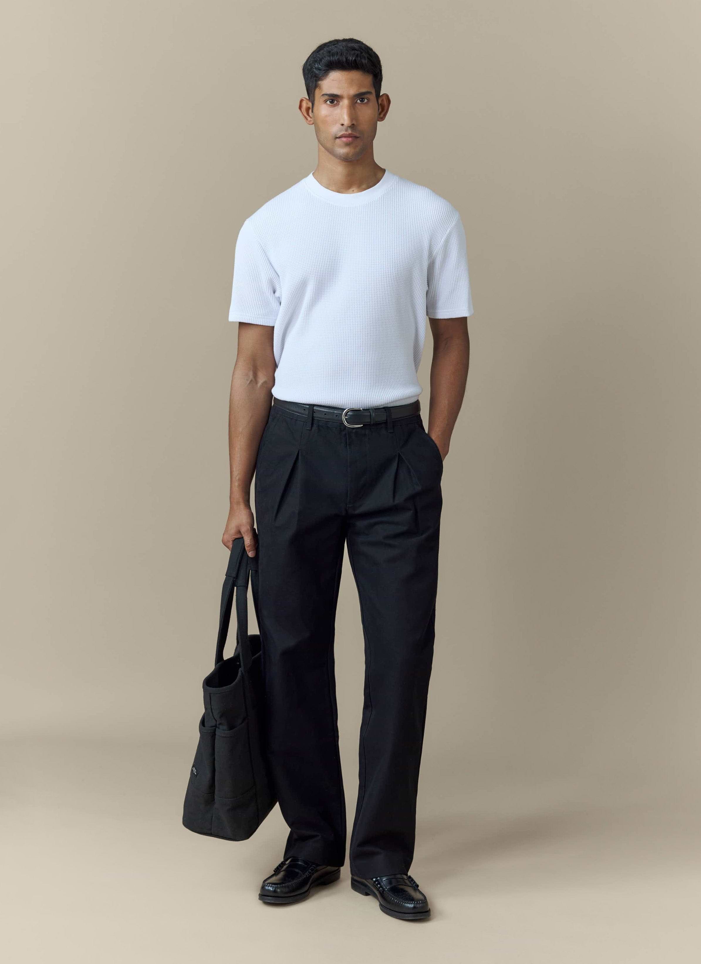 A model wears the Percival Seb Inverted Pleat Trousers in black, styled with a white ribbed t-shirt and black loafers.