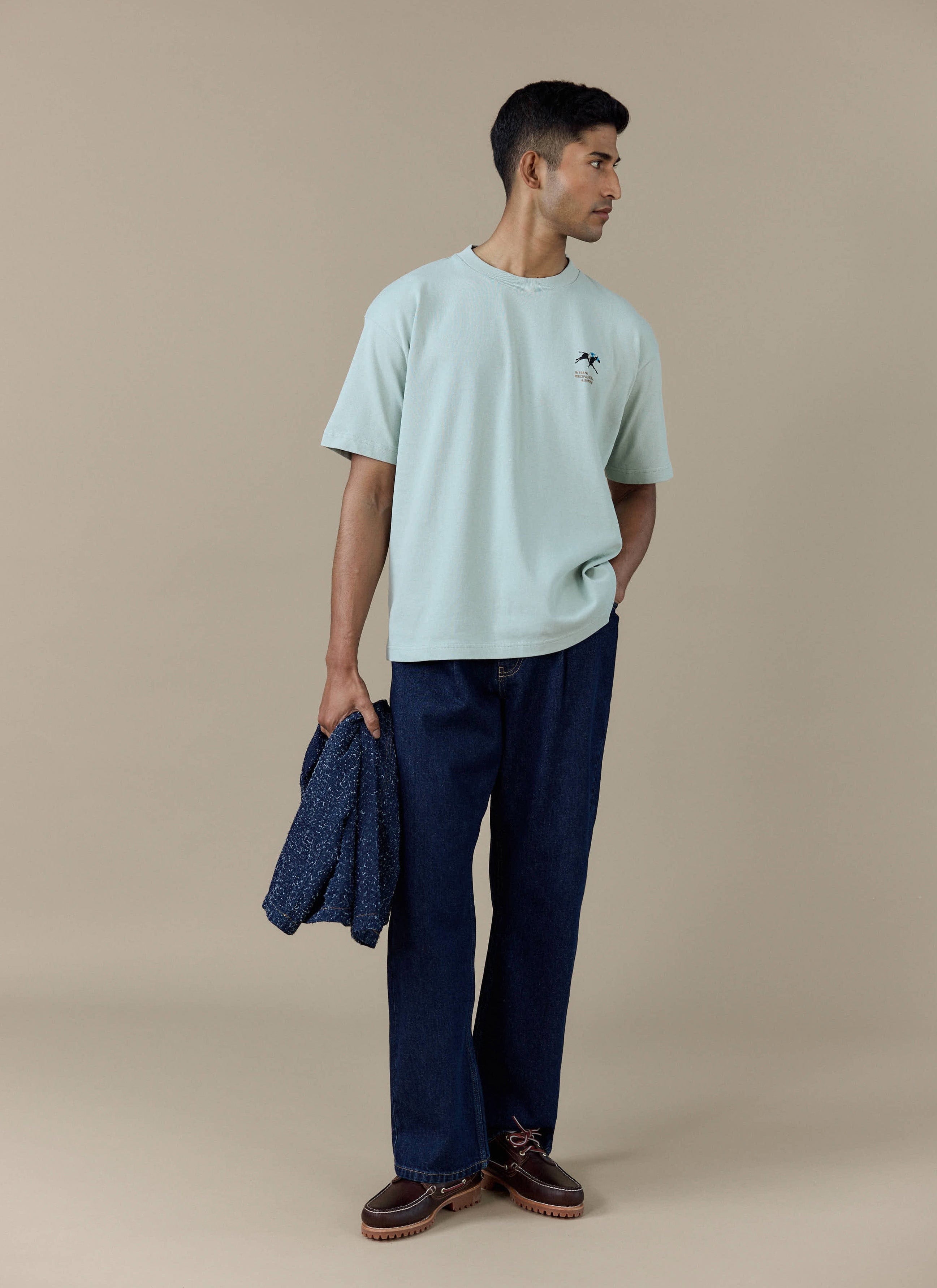 Model wearing the Percival Fair and Show Oversized T Shirt in sage organic cotton, featuring the small chest graphic.
