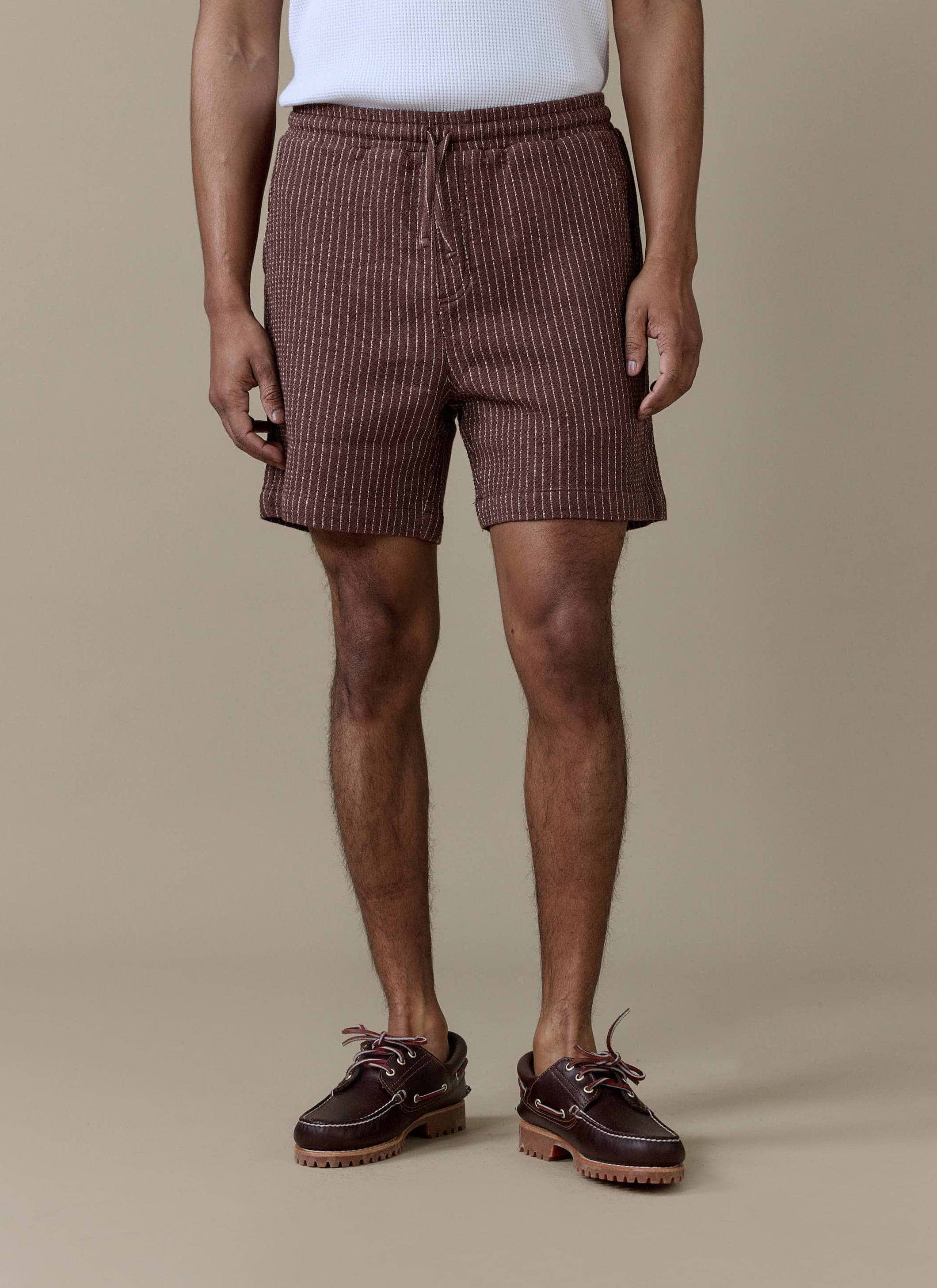 A model wearing the Percival Sorrento Shorts in brown linen, featuring a subtle vertical stripe and drawstring waistband.