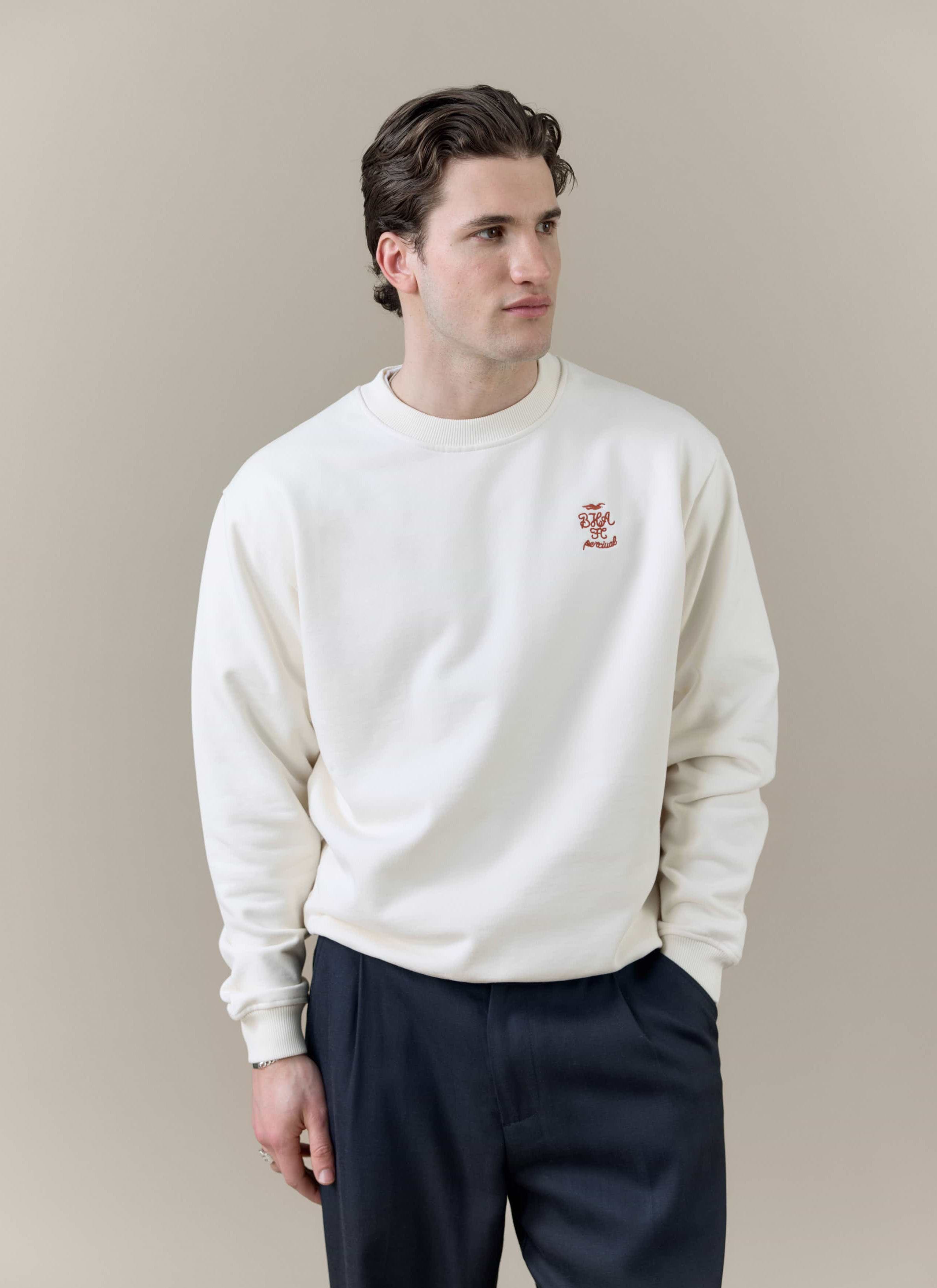 A model wears the Percival x Brighton & Hove Albion F.C. collaboration sweatshirt in cream with navy trousers.