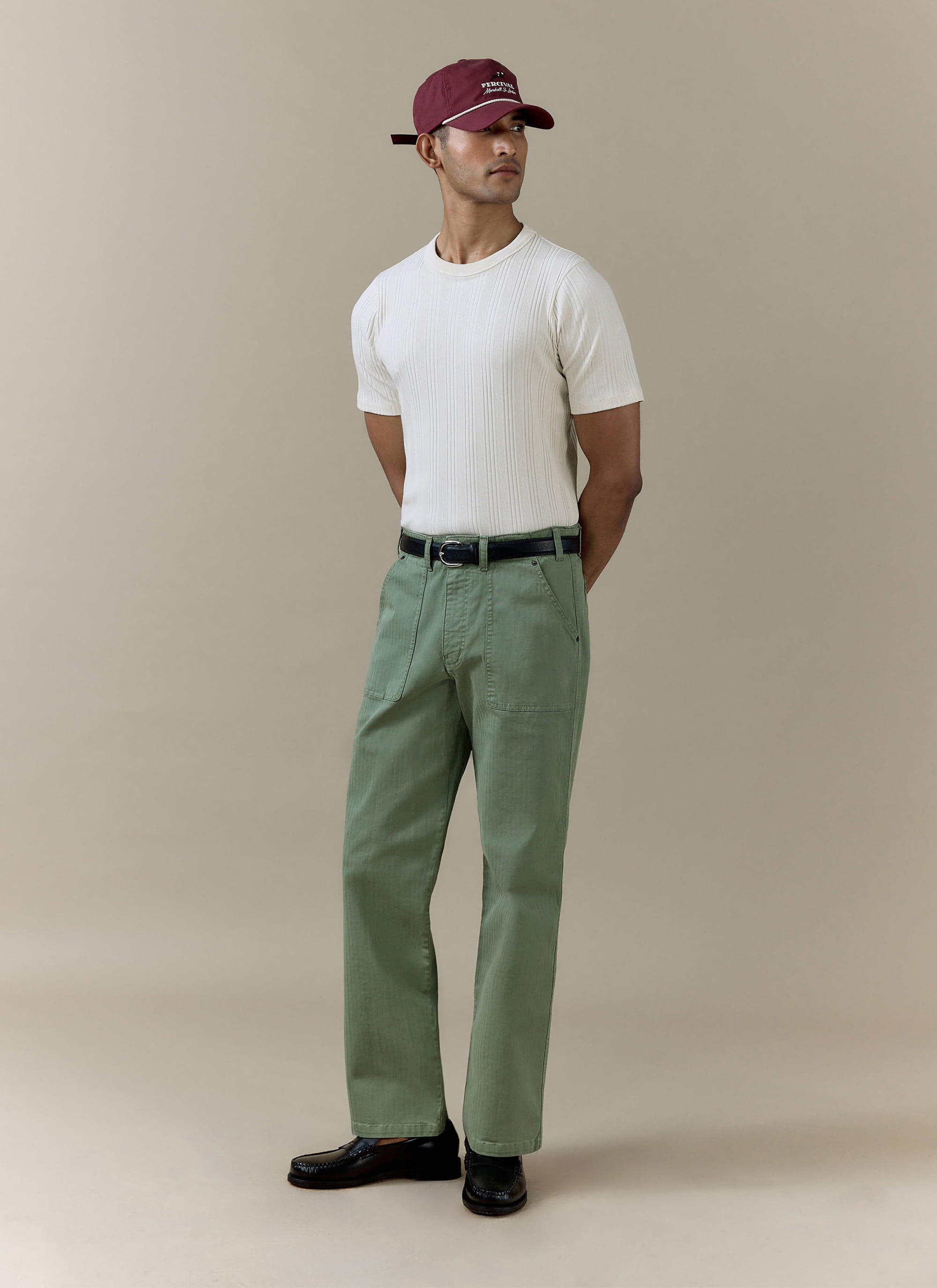 Sage green Percival Lungo Herringbone Straight Trousers in cotton, styled with a white ribbed tee and maroon cap.